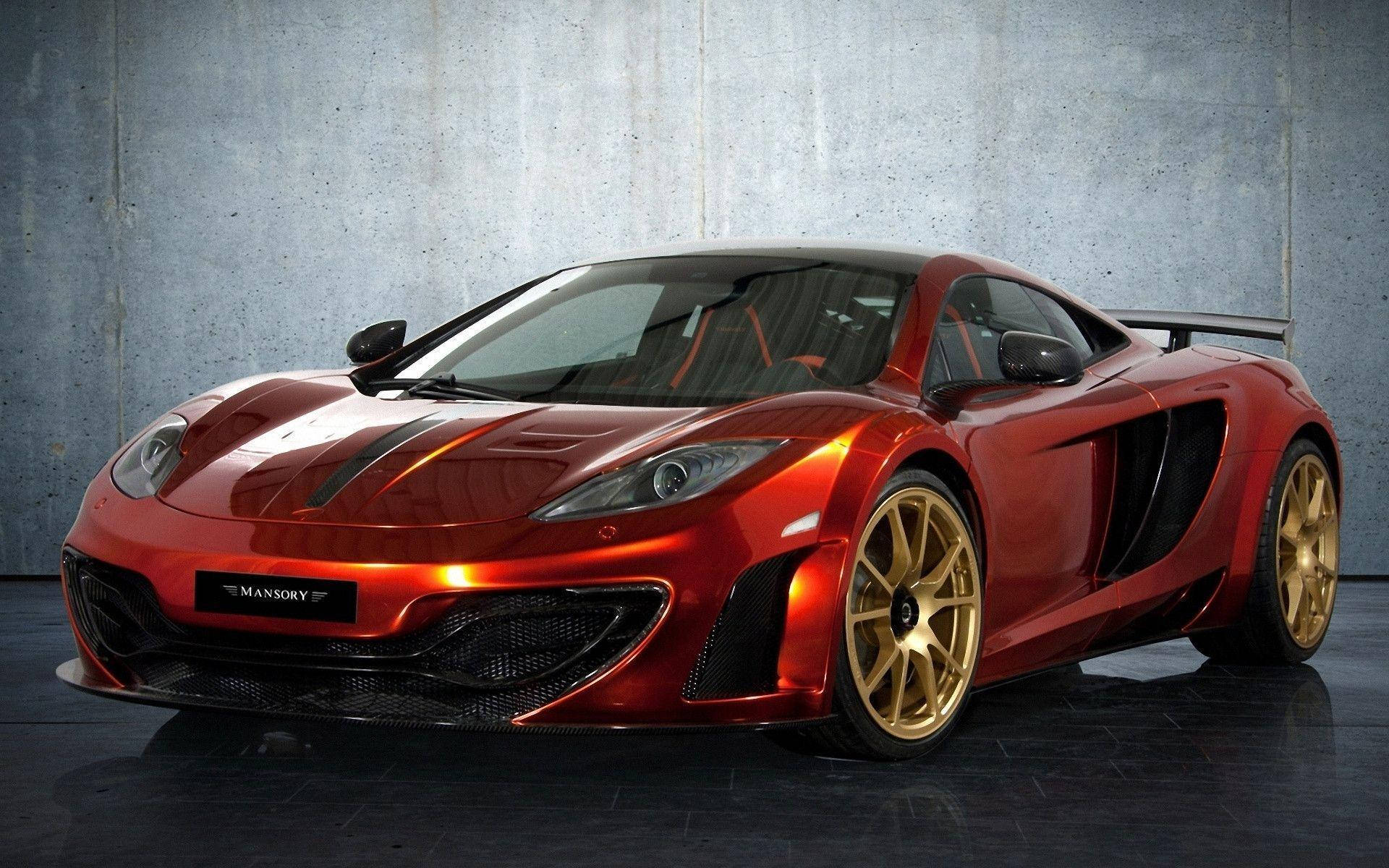 Sports Car 桌布 壁紙 — 一輛光澤的紅色Mansory改裝McLaren跑車，配備金色輪圈，在攝影棚燈光下對著紋理混凝土牆閃耀。