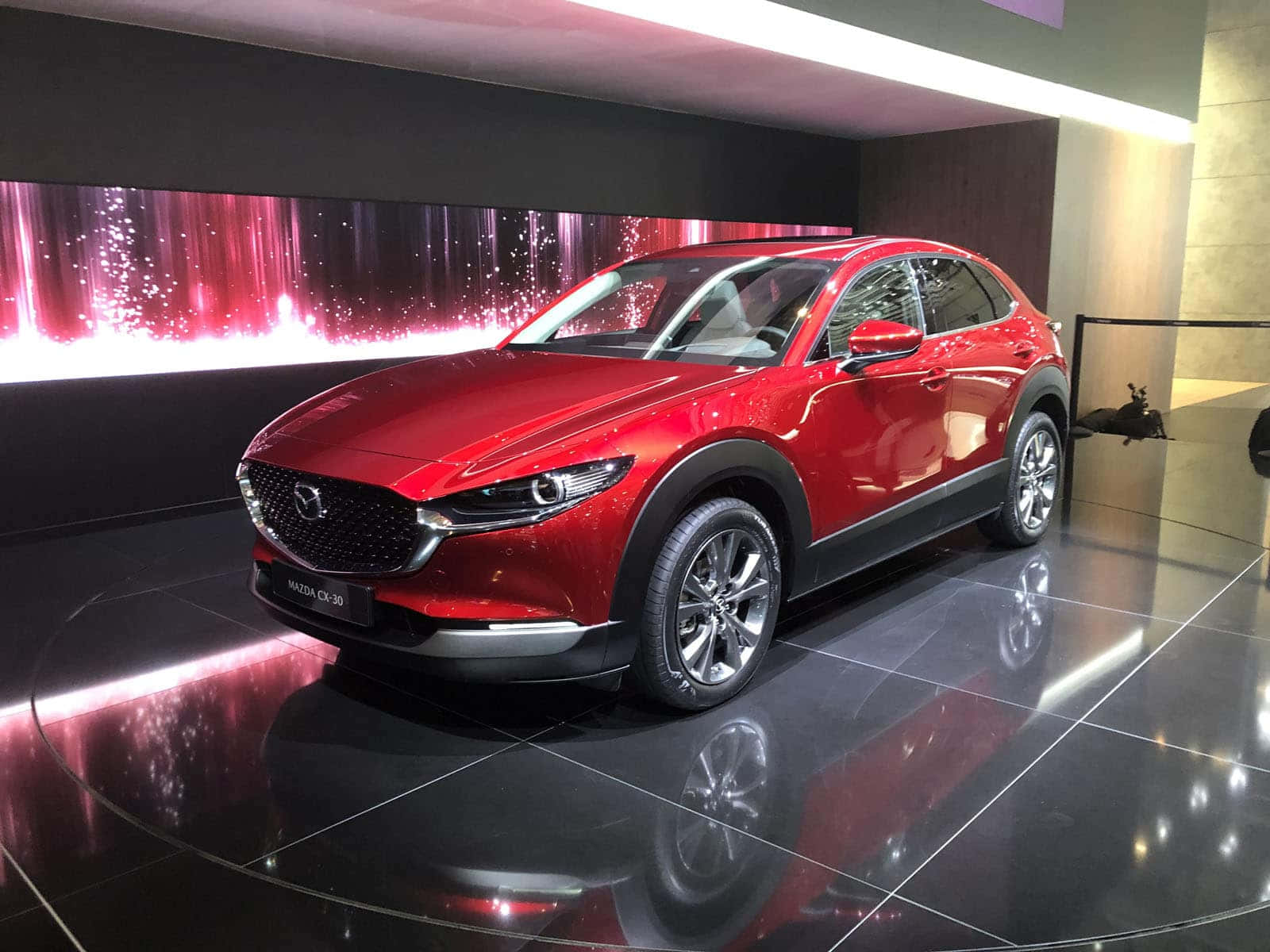 Mazda Cx-30 桌布 壁紙 — 一輛光澤的紅色Mazda CX-30 SUV在攝影棚燈光下，在反射黑色地板上閃耀，背景是閃爍的粉紅色。