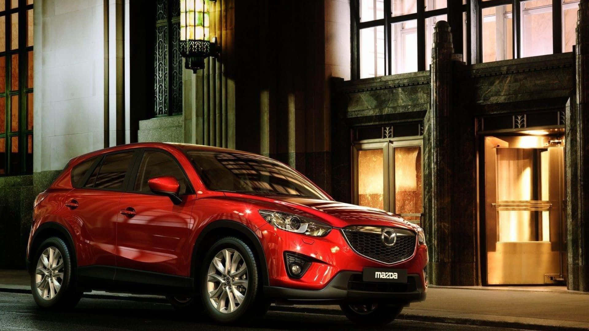 Mazda Cx-5 桌布 壁紙 — 一輛光澤的紅色Mazda CX-5 SUV在夜間停在一棟優雅的建築前，建築物有溫暖發光的窗戶和華麗的建築風格。
