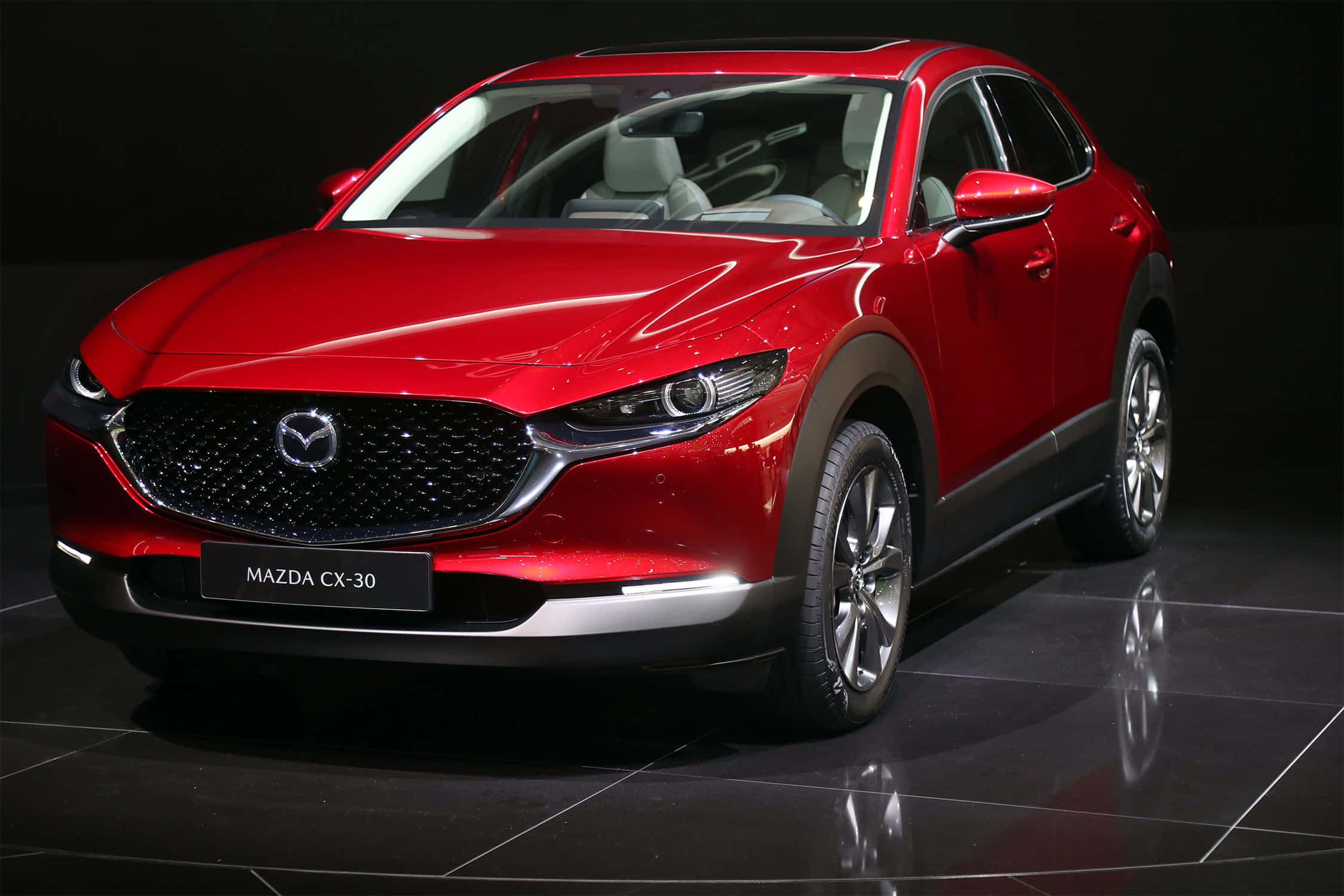 Mazda Cx-30 桌布 壁紙 — 一輛光澤的紅色Mazda CX-30 SUV在暗色瓷磚地板上展示，在攝影棚燈光下可見反射。