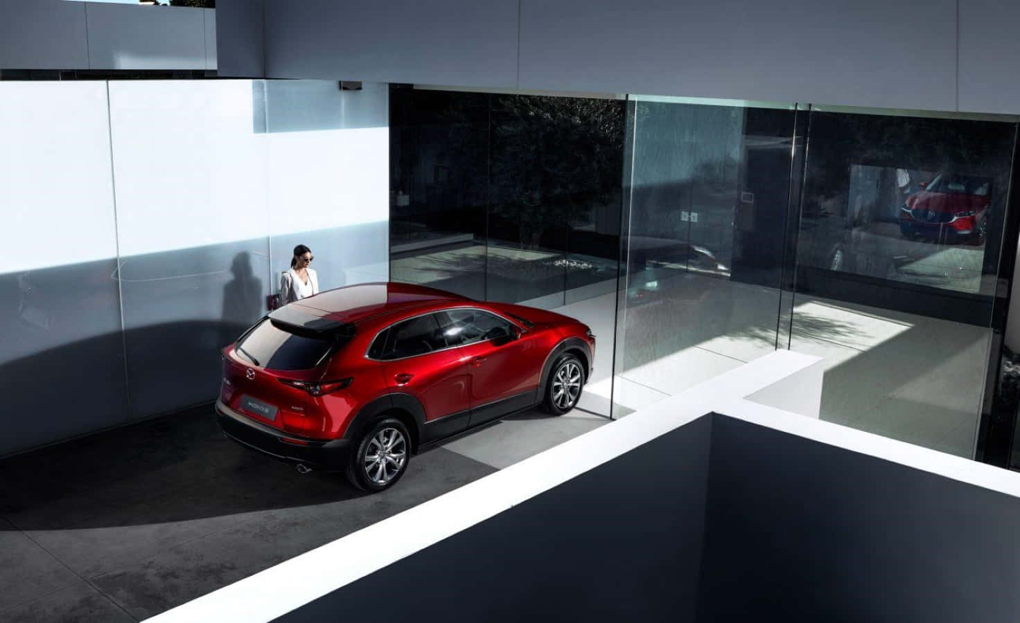 Mazda Cx-30 桌布 壁紙 — 一輛光澤的紅色SUV在現代玻璃牆展廳的明亮燈光下閃耀，附近站著一位女士。
