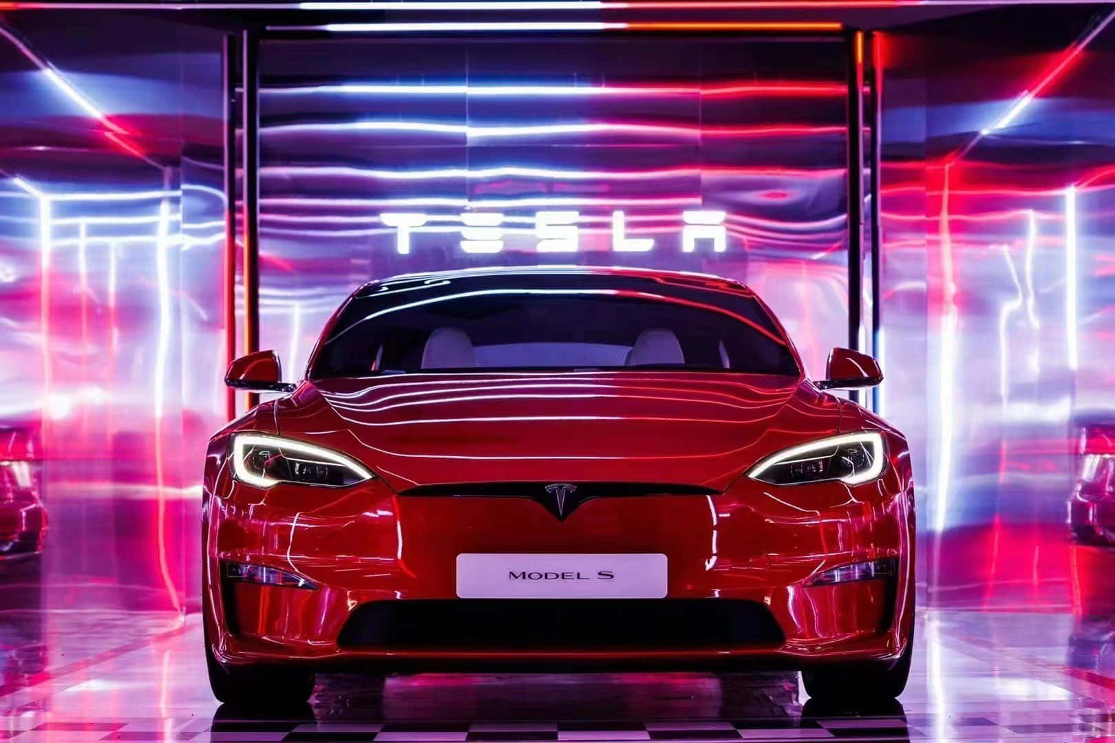 tesla 桌布 壁紙 — 一輛光澤的紅色Tesla Model S在充滿活力的霓虹燈下，於帶有棋盤格地板的未來感展廳中正面朝前。