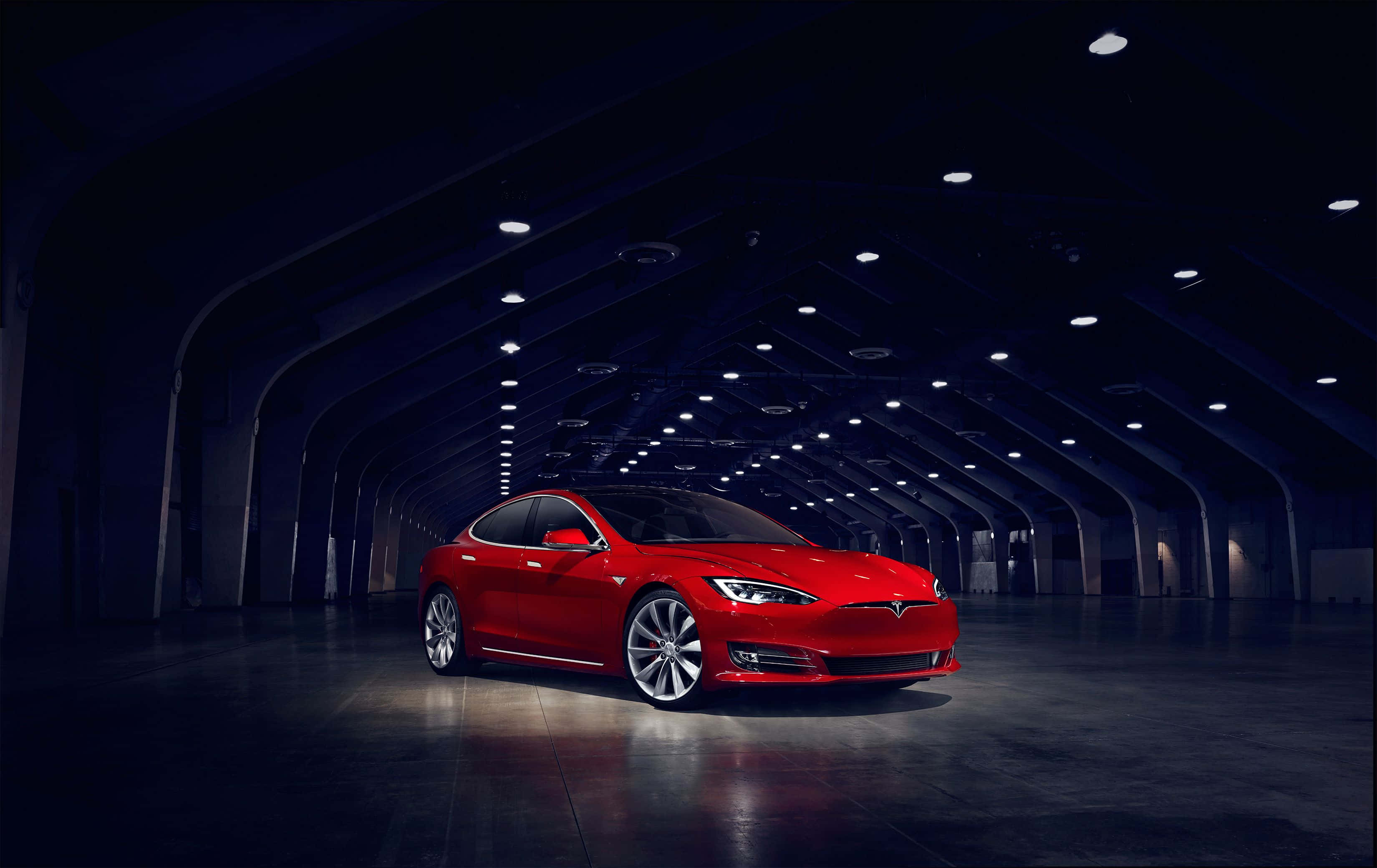 Hybrid Car 桌布 壁紙 — 一輛光澤的紅色Tesla Model S在寬敞黑暗的工業機庫中，拱形天花板下，聚光燈下閃閃發光。