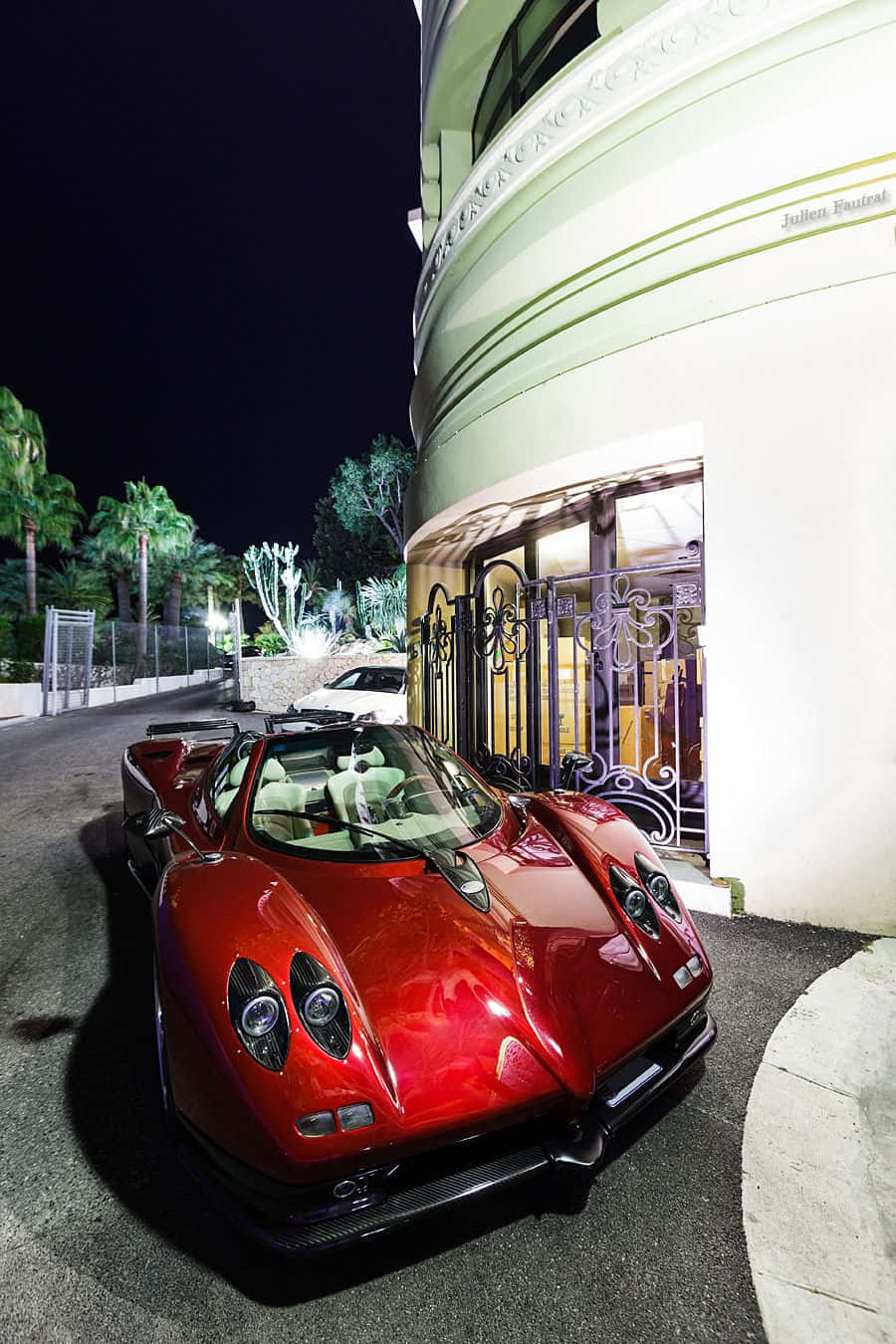 Pagani Zonda C12 Roadster 桌布 壁紙 — 一輛光澤的紅色帕加尼Huayra跑車在夜間停泊在豪華弧形別墅旁，別墅有華麗的大門和棕櫚樹。