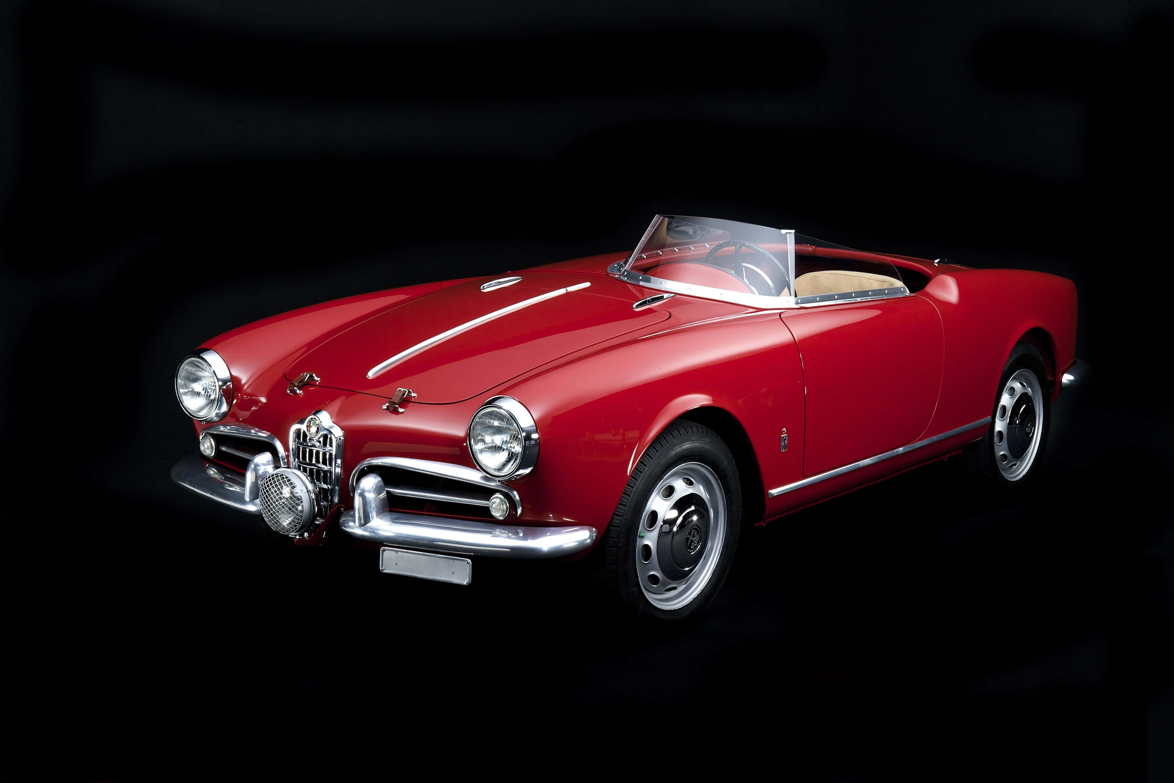 Alfa Romeo Spider 桌布 壁紙 — 一輛光澤的紅色復古Alfa Romeo Spider敞篷車在純黑色背景的攝影棚燈光下閃閃發光。