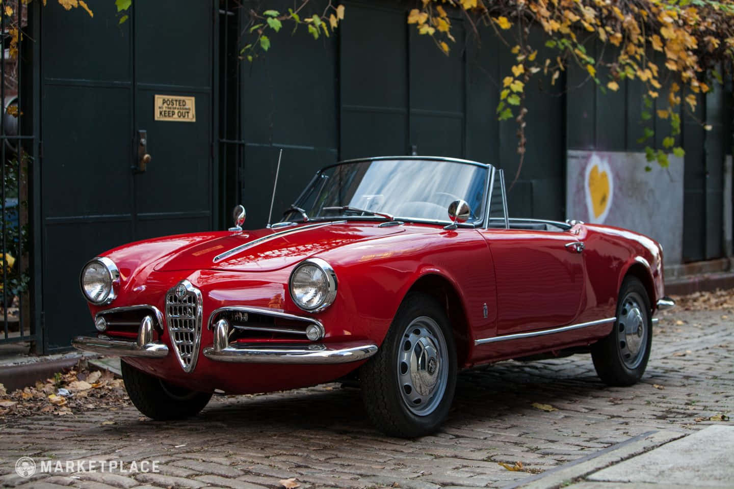 Alfa Romeo Spider 桌布 壁紙 — 一輛光澤的紅色復古愛快羅密歐Spider開篷車停泊在鵝卵石街道上，上方有秋葉。
