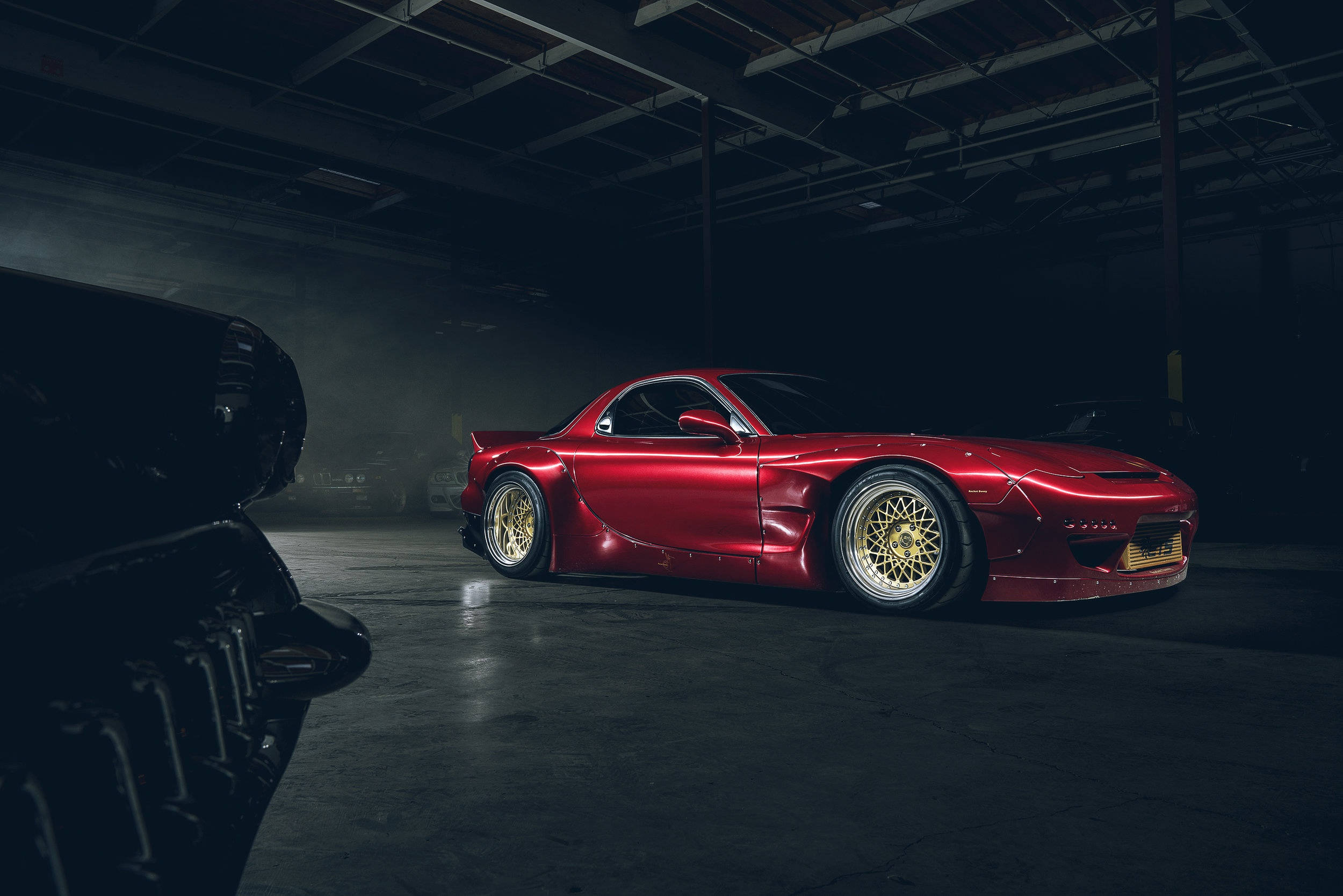Mazda 桌布 壁紙 — 一輛光澤的紅色改裝跑車配金色輪圈，在昏暗的工業車庫中於戲劇性燈光下閃耀。