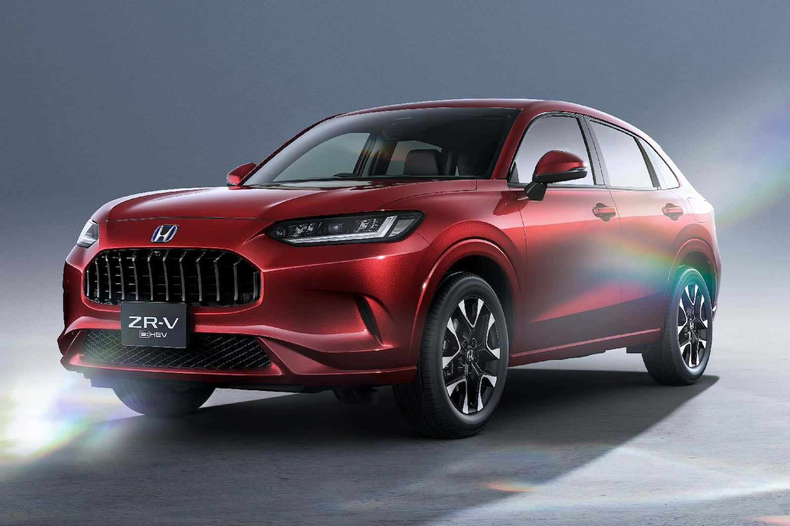 Honda Hr-v 桌布 壁紙 — 一輛光澤的紅色本田ZR-V SUV在攝影棚燈光下閃耀，帶有彩虹鏡頭光暈，背景為灰色漸變。