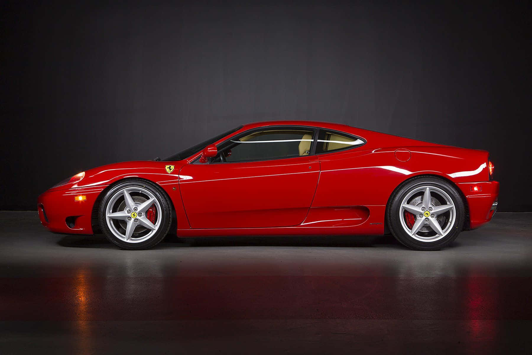 Ferrari 360 Modena 桌布 壁紙 — 一輛光澤的紅色法拉利360跑車在攝影棚燈光下閃耀，背景為深色，地板具有反射效果。