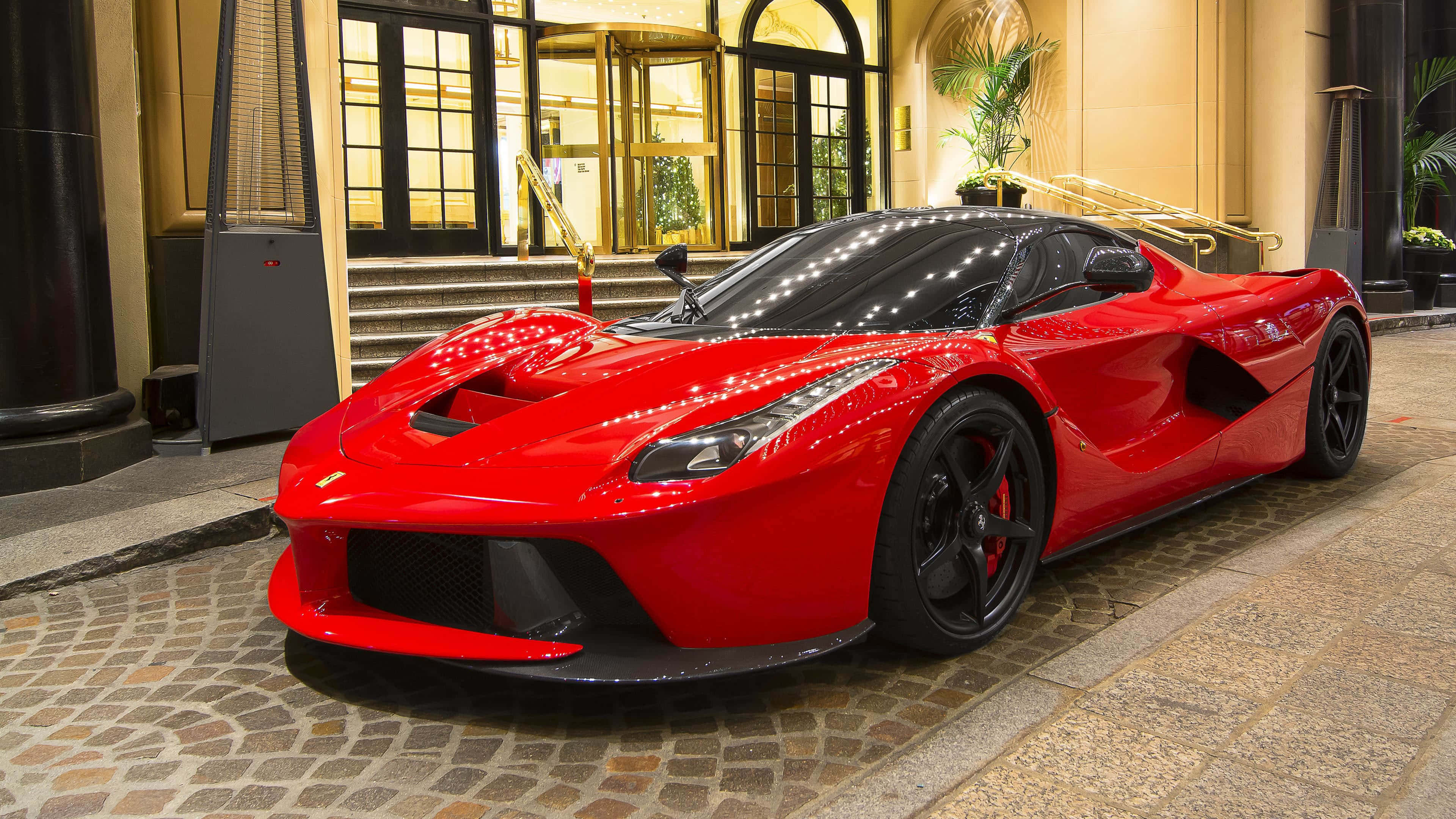Ferrari Laferrari 桌布 壁紙 — 一輛光澤的紅色法拉利LaFerrari超級跑車在溫暖的燈光下閃耀，停在大酒店入口前的鵝卵石車道上。