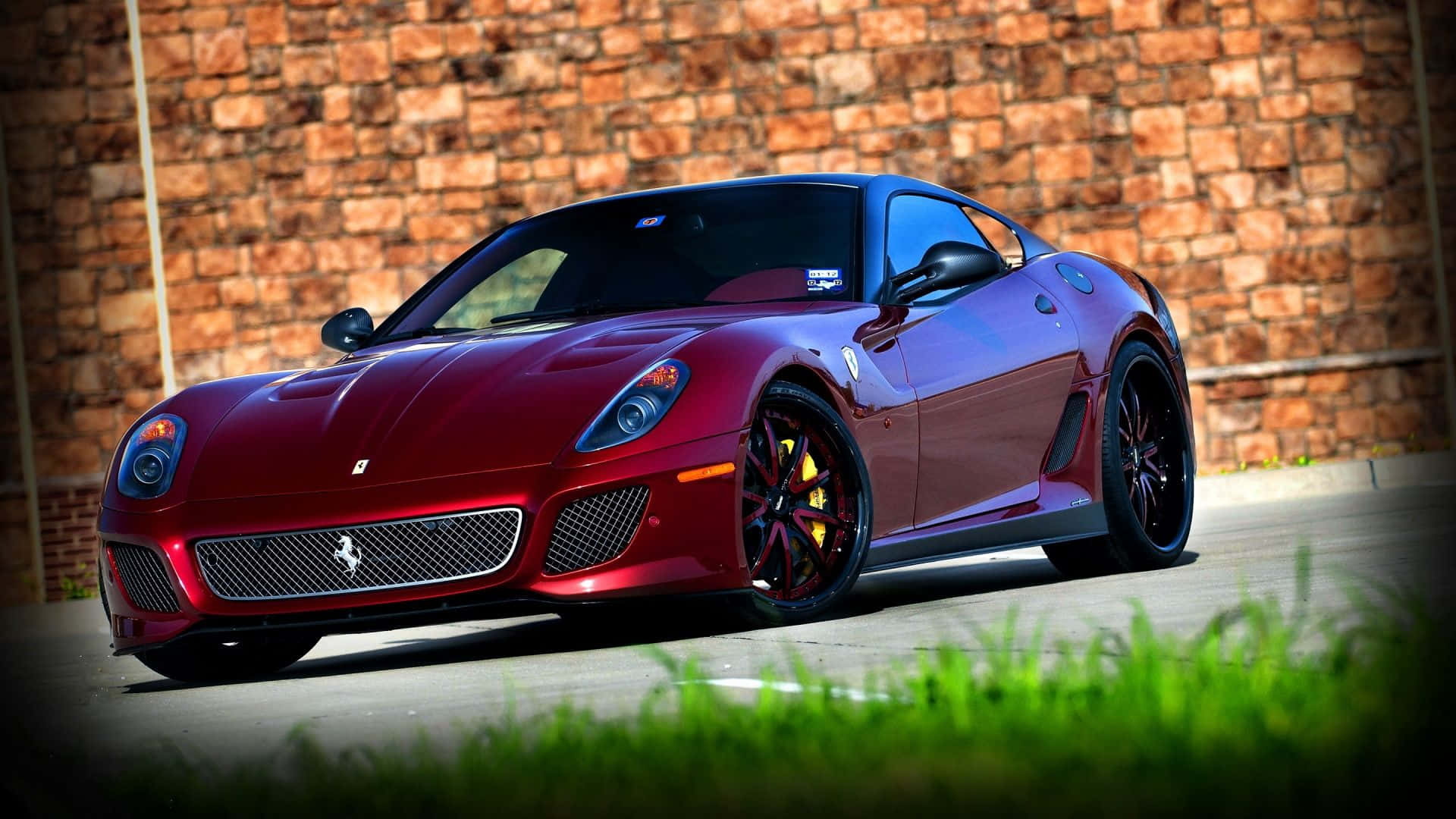 Ferrari 599 Gtb Fiorano 桌布 壁紙 — 一輛光澤的紅色法拉利跑車停泊在風化的磚牆前，前景有充滿活力的綠色草地。