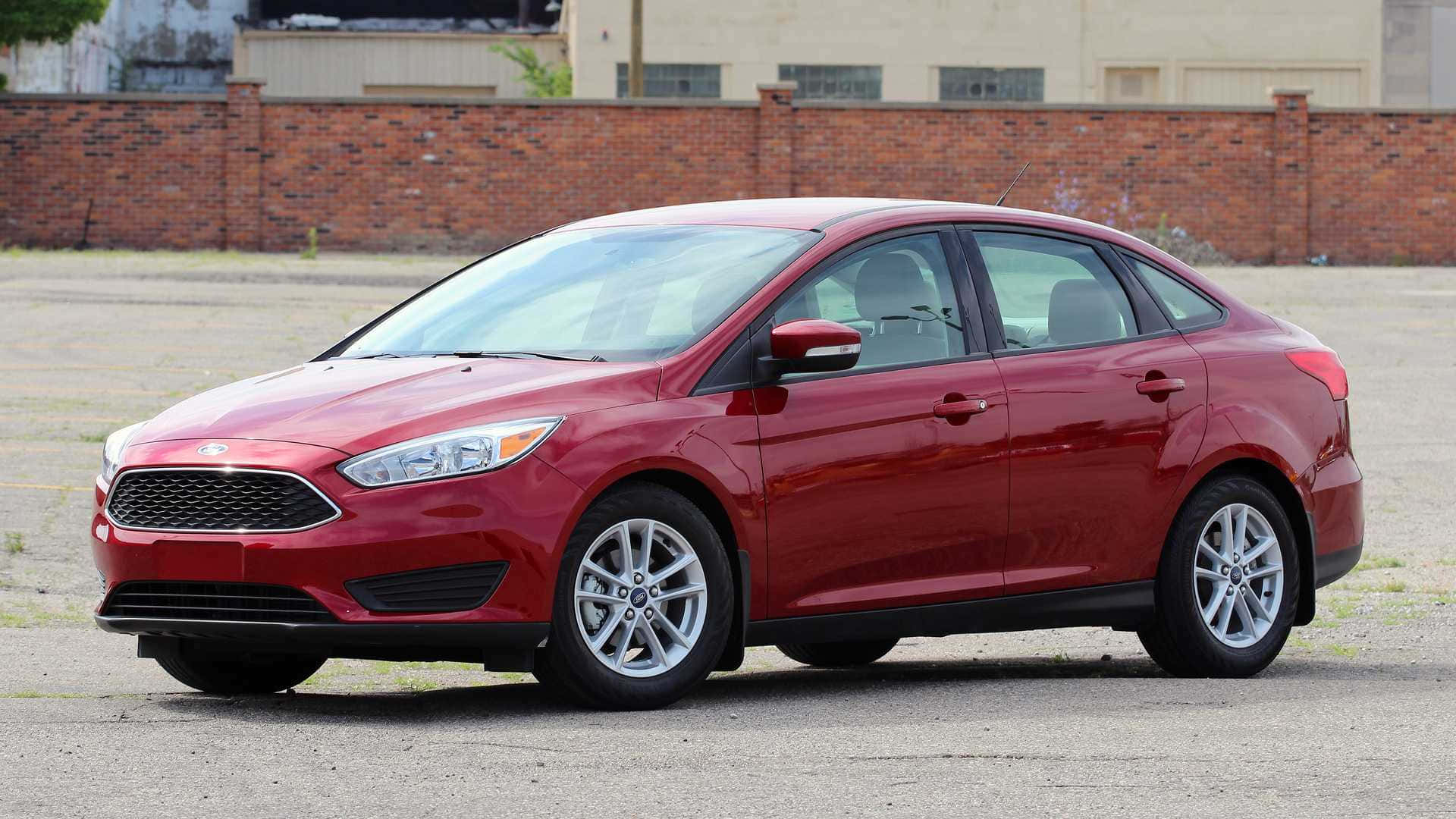 Ford Focus 桌布 壁紙 — 一輛光澤的紅色福特福克斯轎車停在瀝青上，背景有磚牆和工業建築。