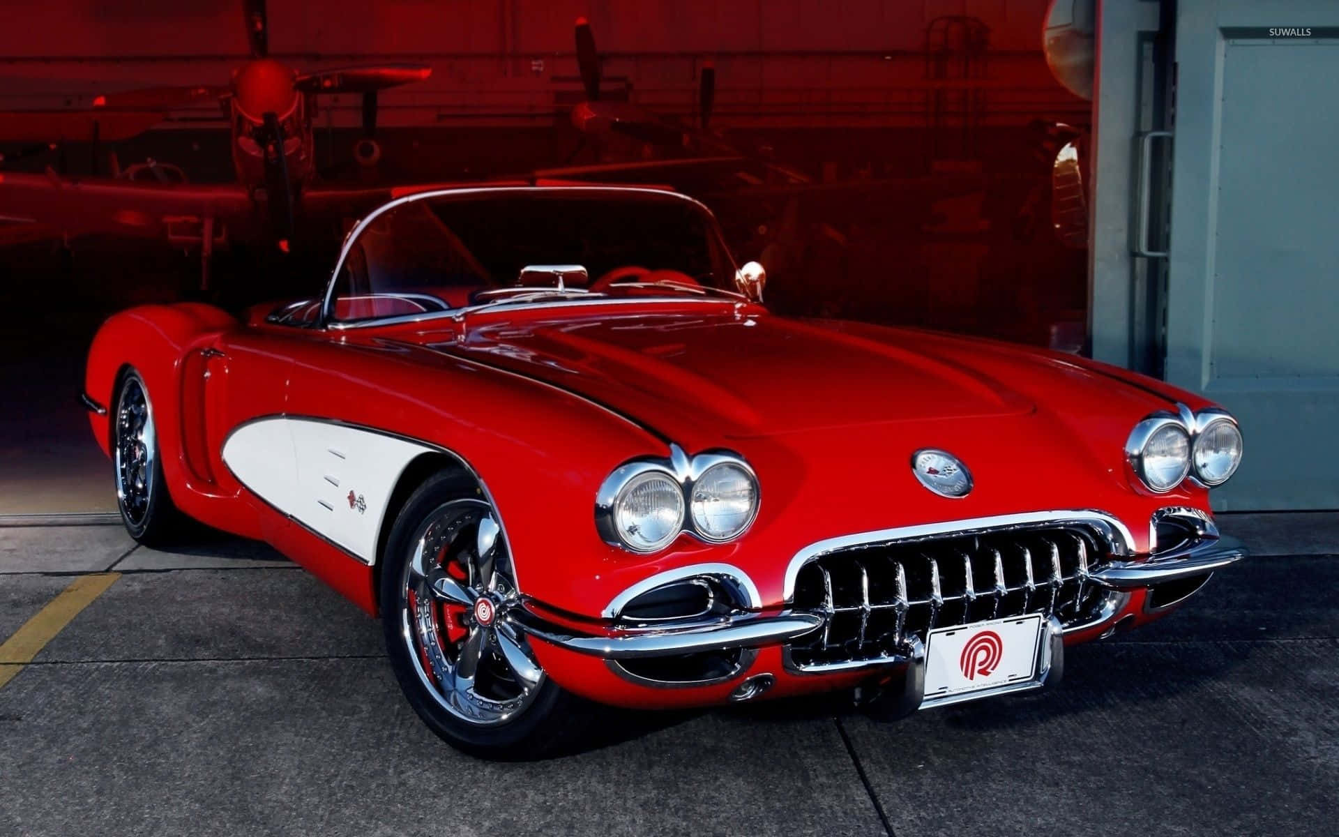 classic 桌布 壁紙 — 一輛光澤的紅色經典Corvette敞篷車帶有白色側條紋，在溫暖的車庫燈光下閃閃發光。
