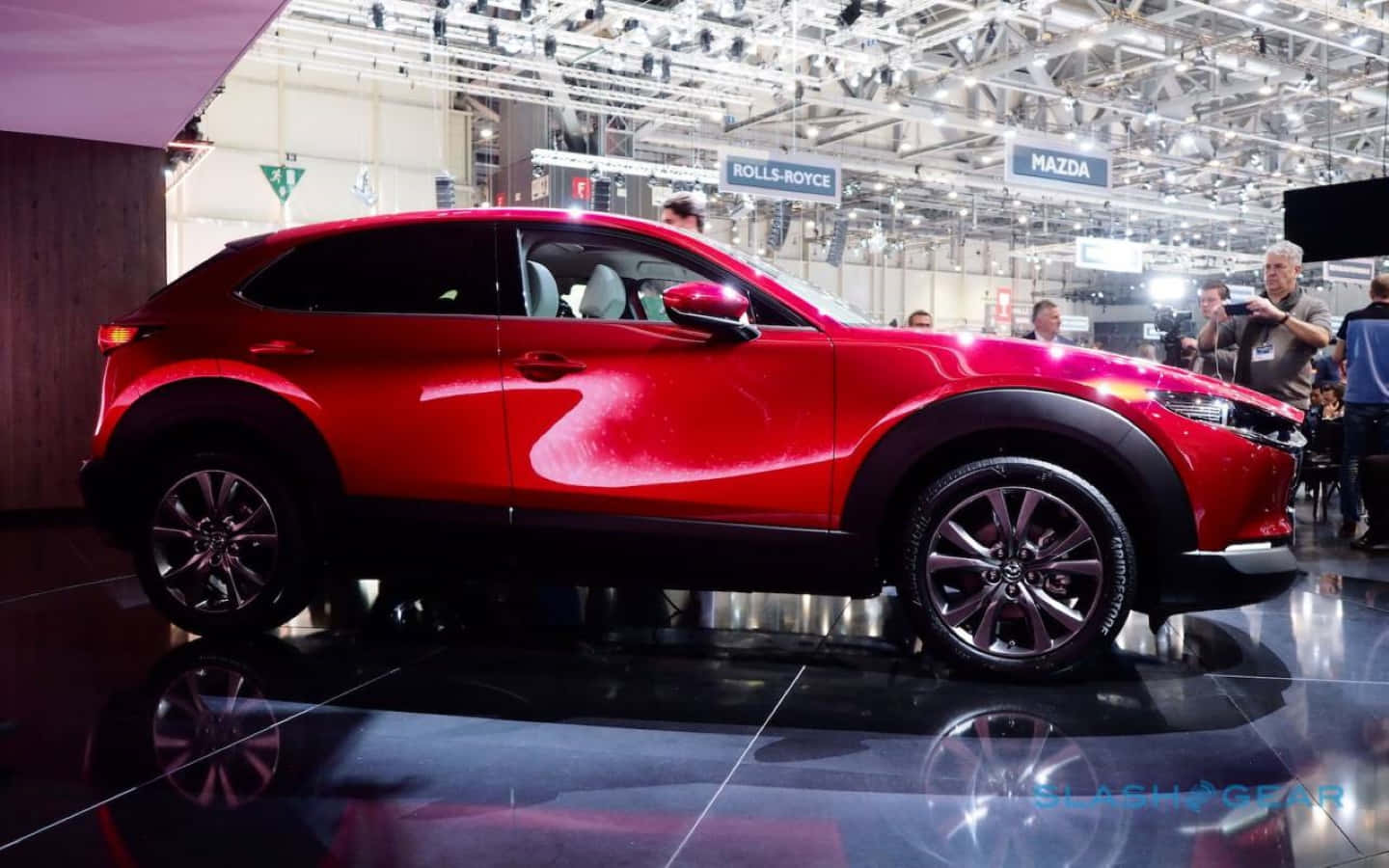 Mazda Cx-30 桌布 壁紙 — 一輛光澤的紅色萬事得CX-30 SUV在車展的反射地板上，在明亮的展覽燈光下閃閃發光。