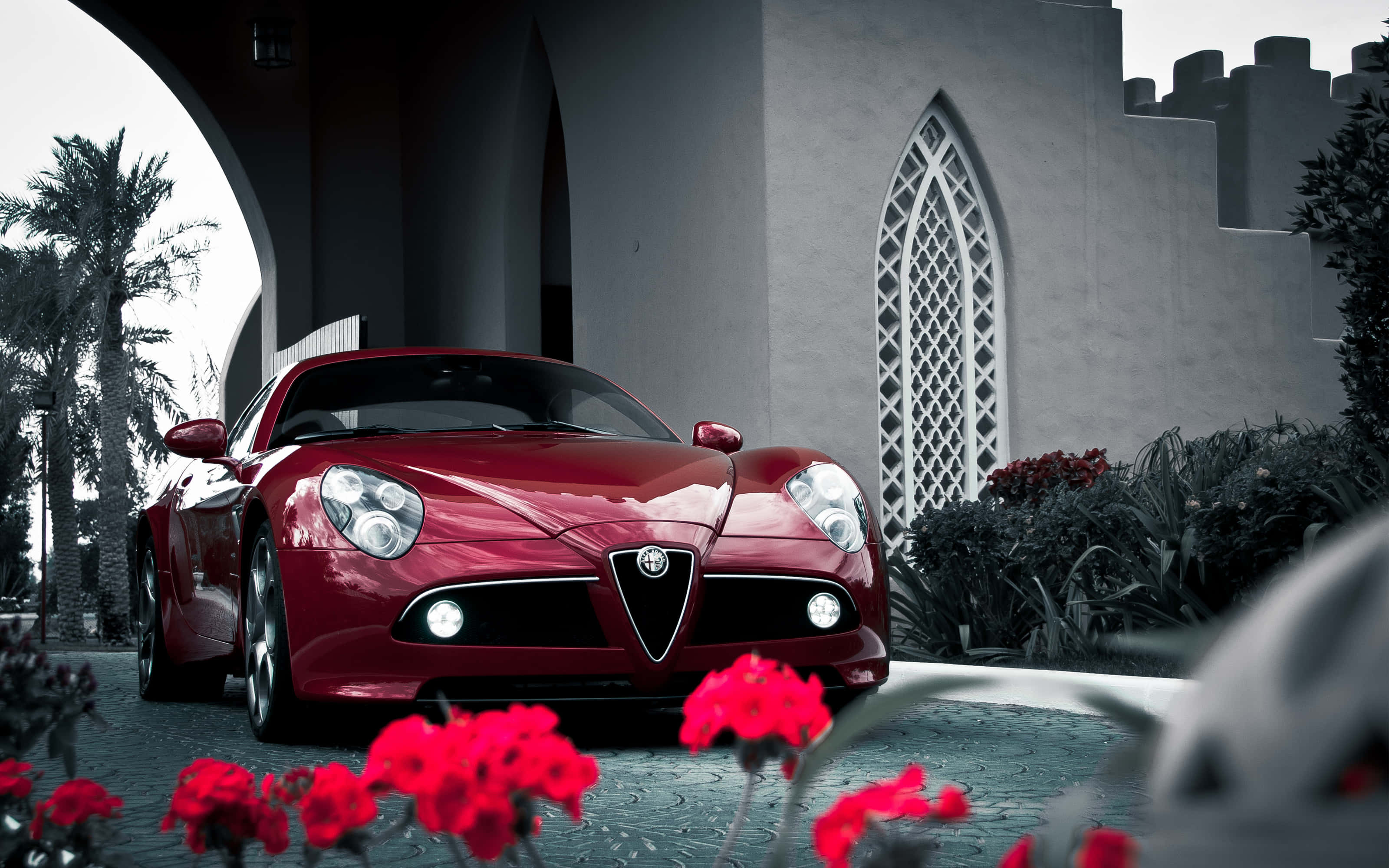 Alfa Romeo 8c Competizione 桌布 壁紙 — 一輛光澤的紅色跑車停放在石拱門下，前景有鮮豔的紅花，背景是哥德式建築。