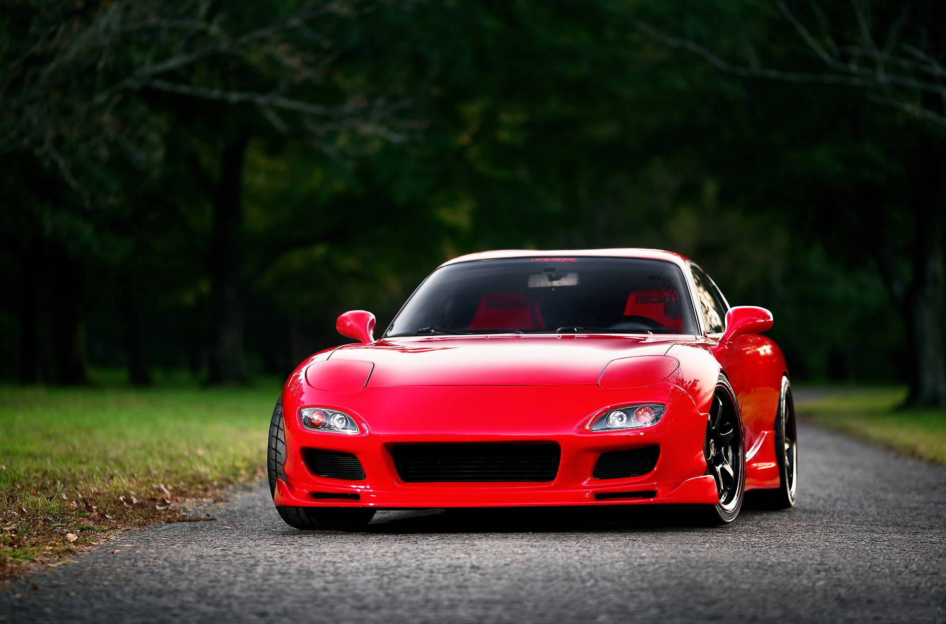 Mazda 桌布 壁紙 — 一輛光澤的紅色跑車配黑色輪圈，在柔和自然光下停在兩旁樹木的瀝青路中央。
