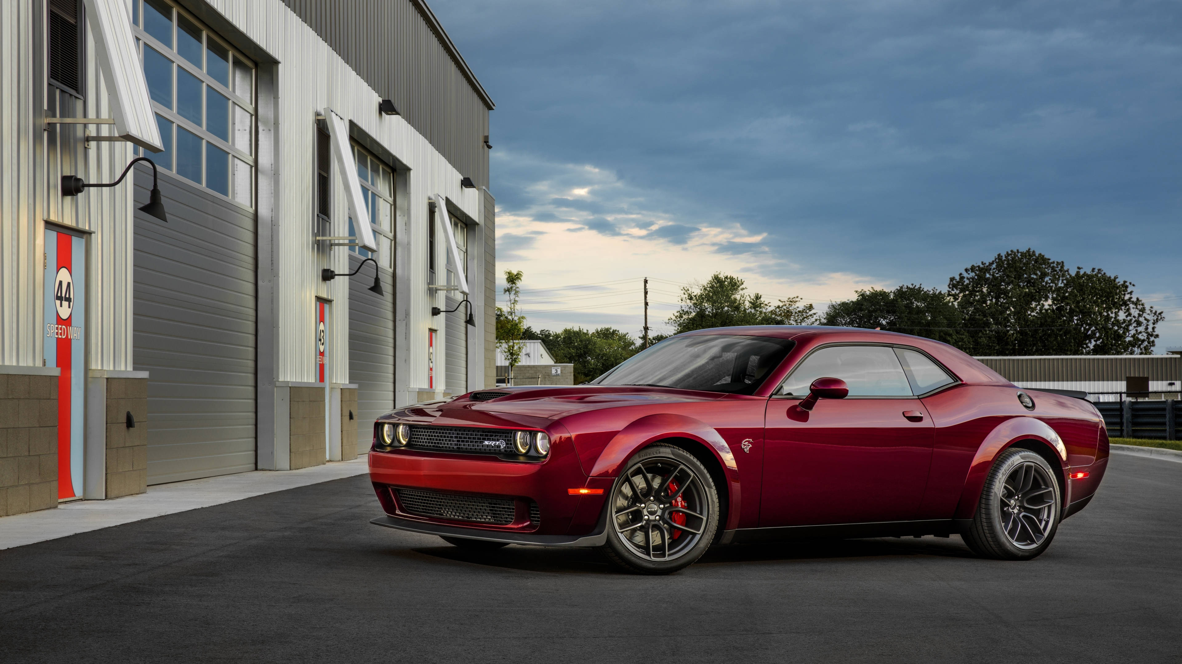Dodge 桌布 壁紙 — 一輛光澤的紅色道奇挑戰者肌肉車停放在現代工業車庫前，天空多雲，暮色蒼茫。