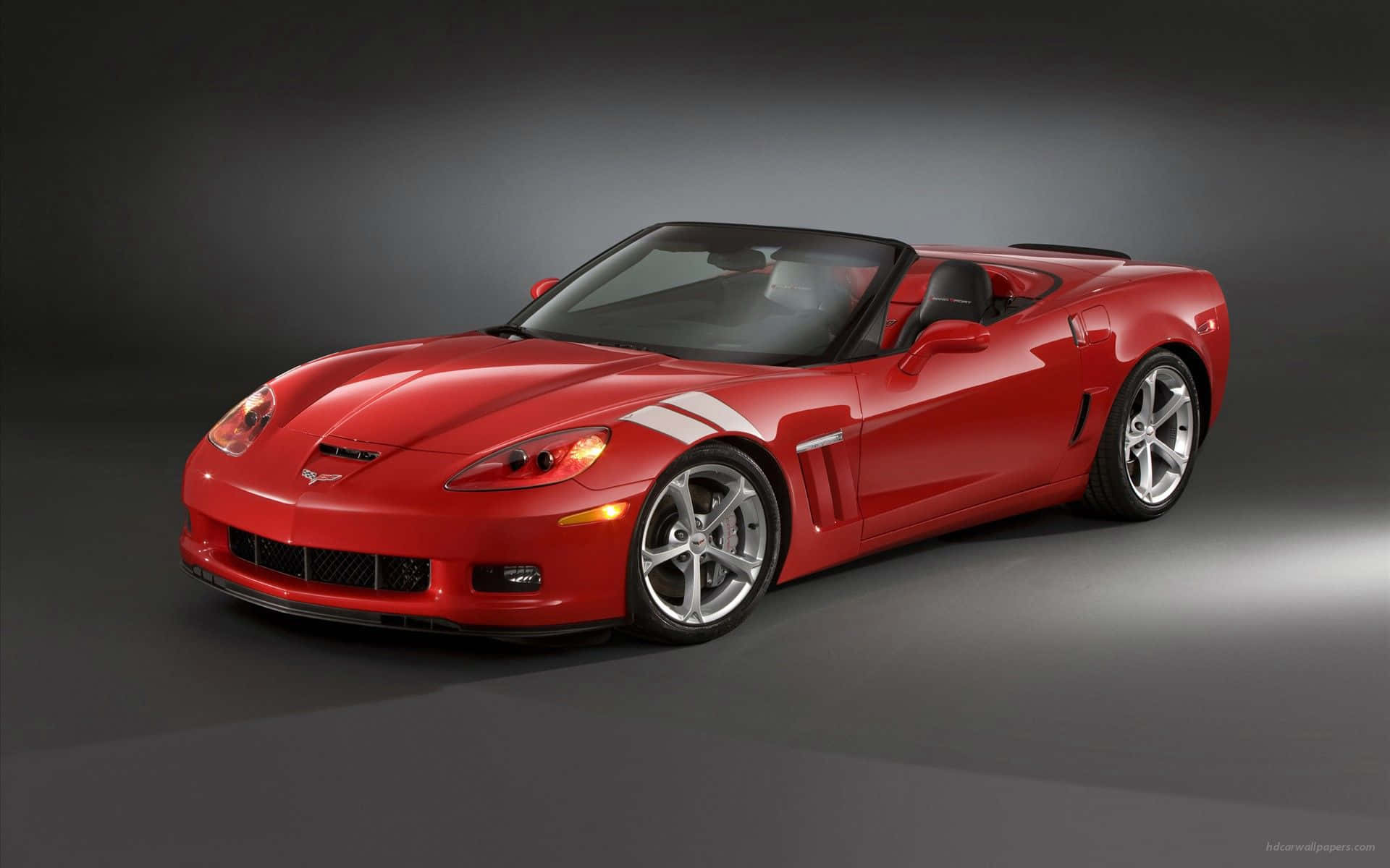 Chevrolet Corvette Grand Sport 桌布 壁紙 — 一輛光澤的紅色雪佛蘭克爾維特敞篷車，帶有白色賽車條紋，在深灰色背景的攝影棚燈光下閃閃發光。