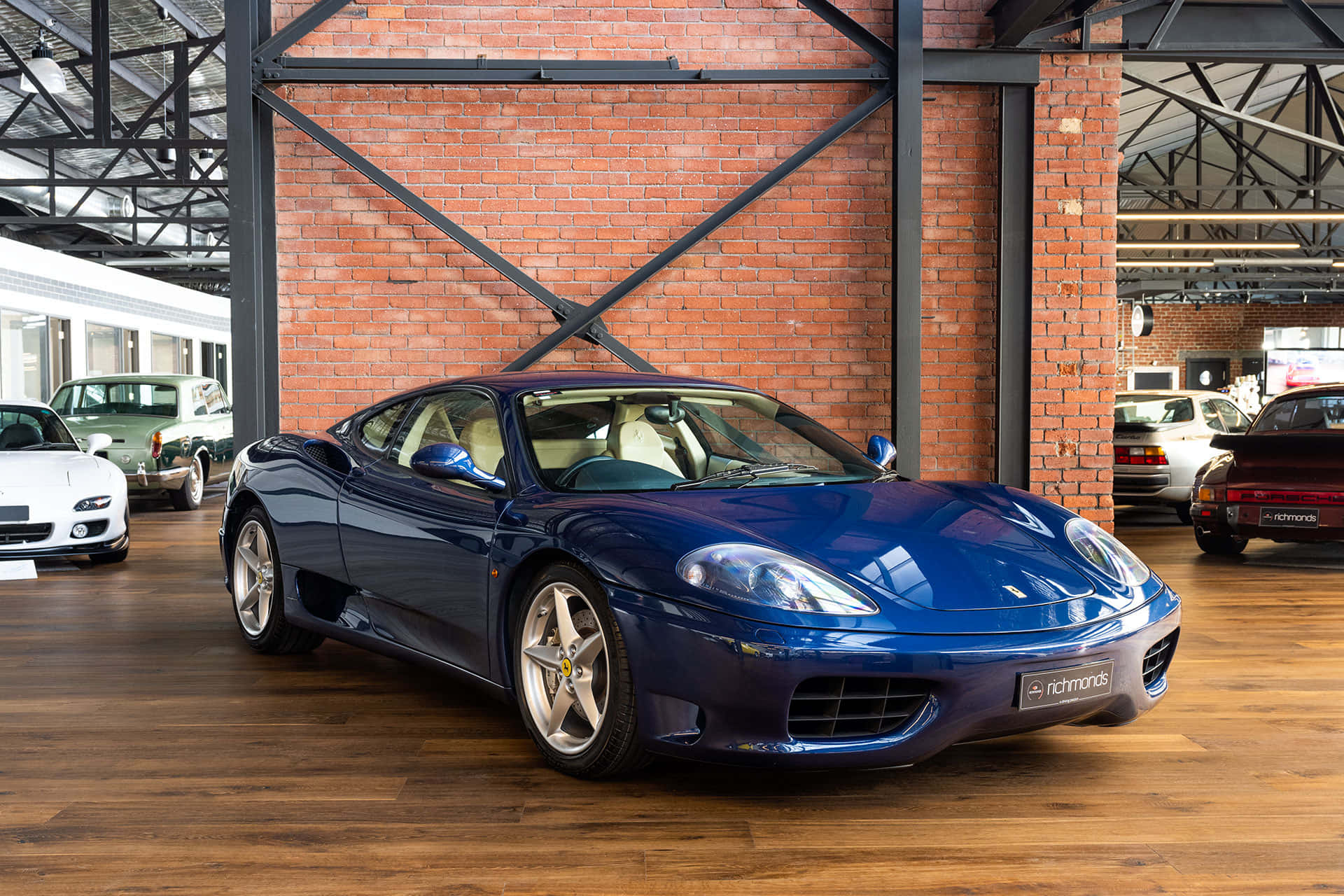 Ferrari F430 桌布 壁紙 — 一輛光澤的藍色法拉利360跑車在質樸的磚鐵倉庫展廳內，在明亮的燈光下閃閃發光。