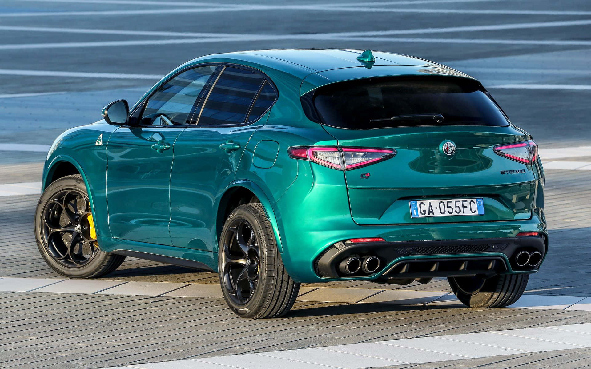 Alfa Romeo Stelvio 桌布 壁紙 — 一輛光澤的青綠色Alfa Romeo Stelvio Quadrifoglio SUV停泊在鋪砌路面上，配有大膽的黑色輪圈和四出排氣管。