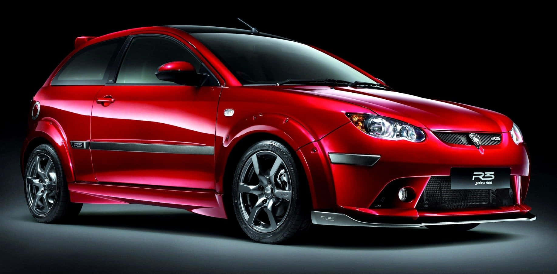Proton 桌布 壁紙 — 一輛光澤紅色跑車，帶有黑色飾件和銀色輪圈，在深色工作室背景前展示。