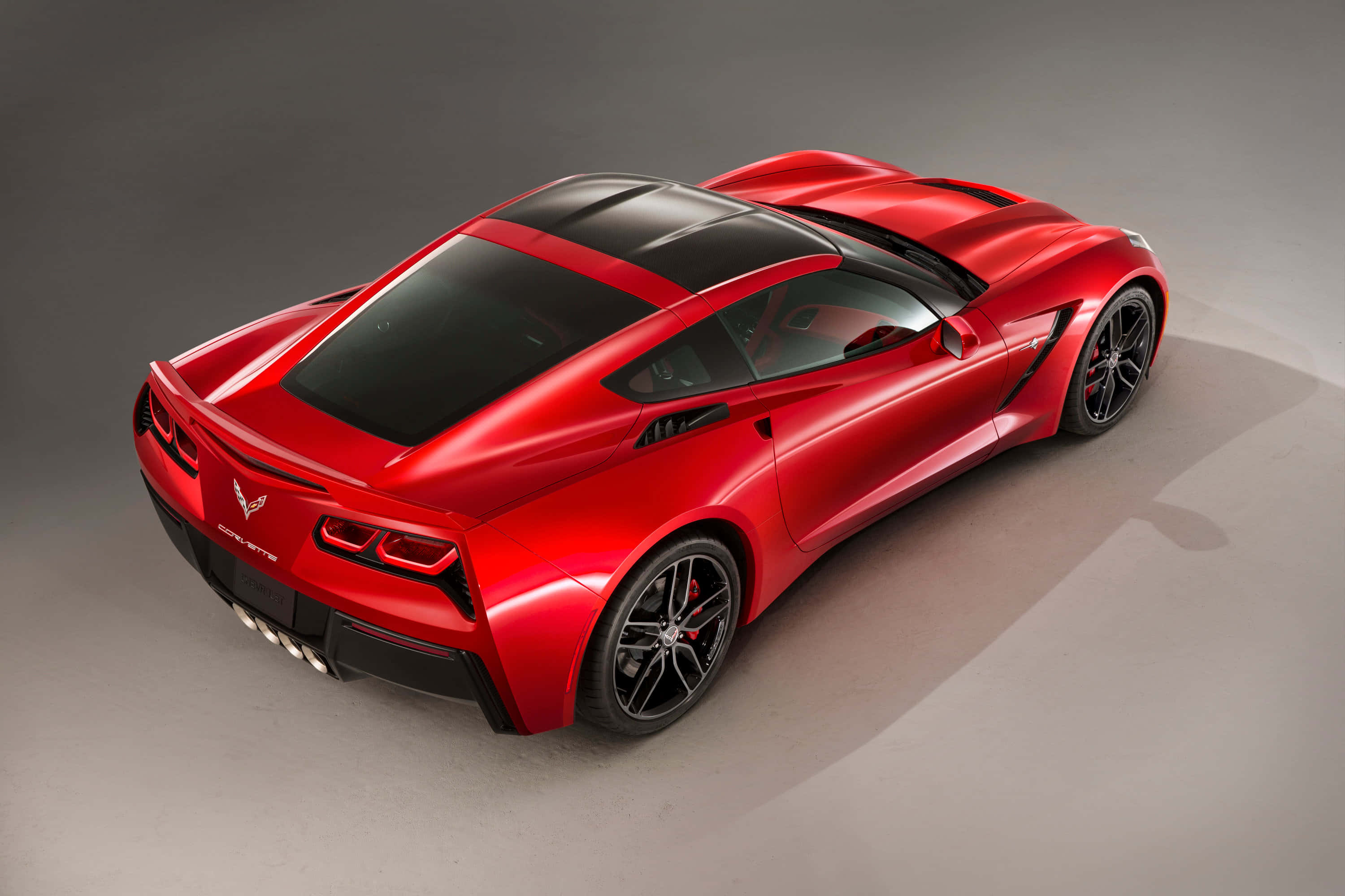 Chevrolet Corvette Stingray 桌布 壁紙 — 一輛光澤紅色雪佛蘭Corvette跑車，帶有黑色飾件和時尚設計，從高角度在中性工作室地板上觀看。