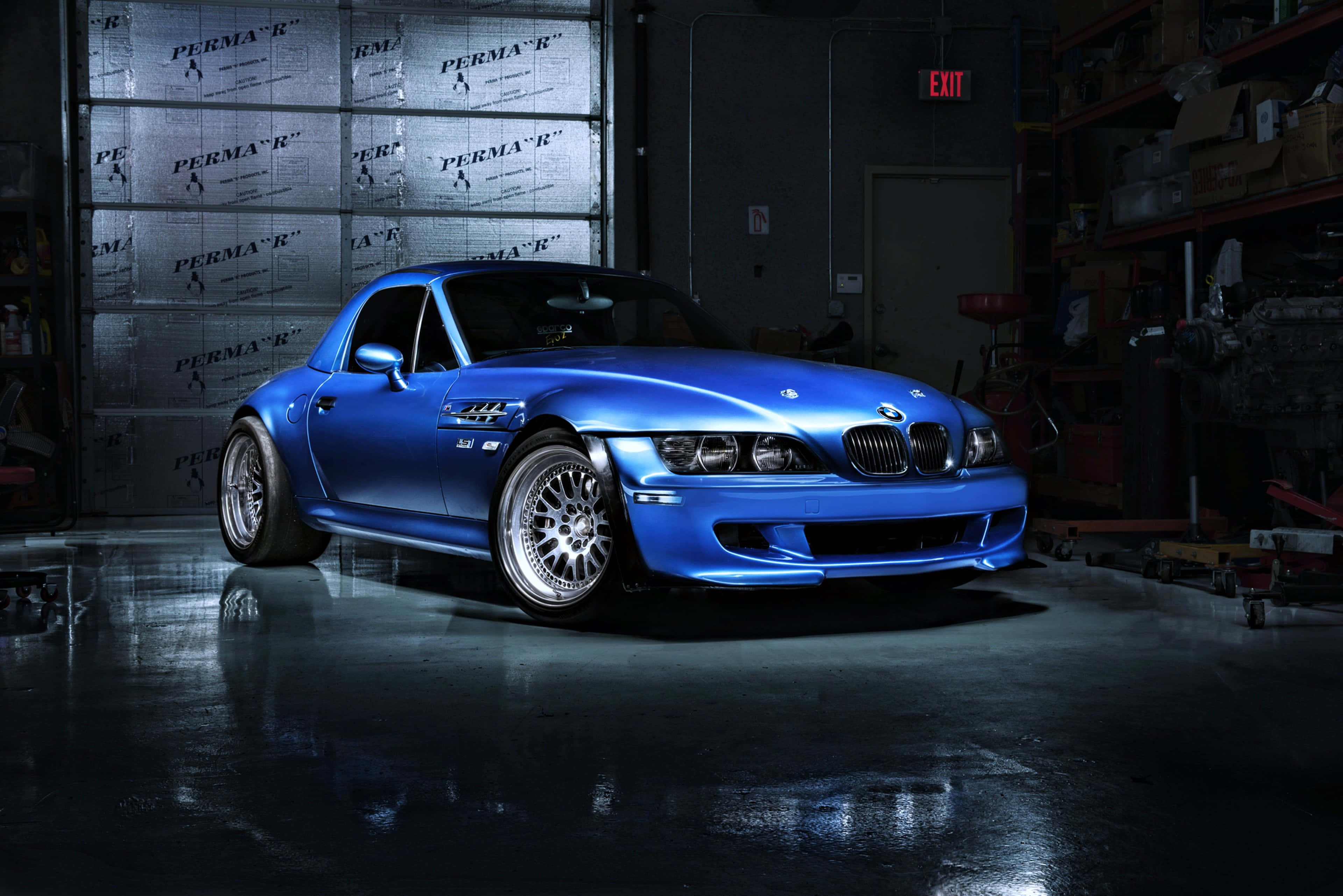 Bmw Z3 桌布 壁紙 — 一輛光澤藍色BMW Z3跑車在昏暗車庫中，聚光燈下閃耀，濕滑地面反射光線。