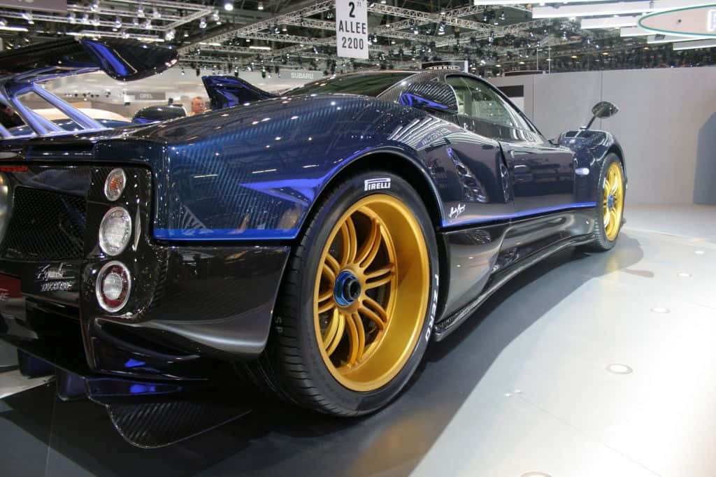 Pagani Zonda Tricolore 桌布 壁紙 — 一輛光澤藍色Pagani Zonda跑車配金色輪圈，在明亮燈光下的車展中展出。