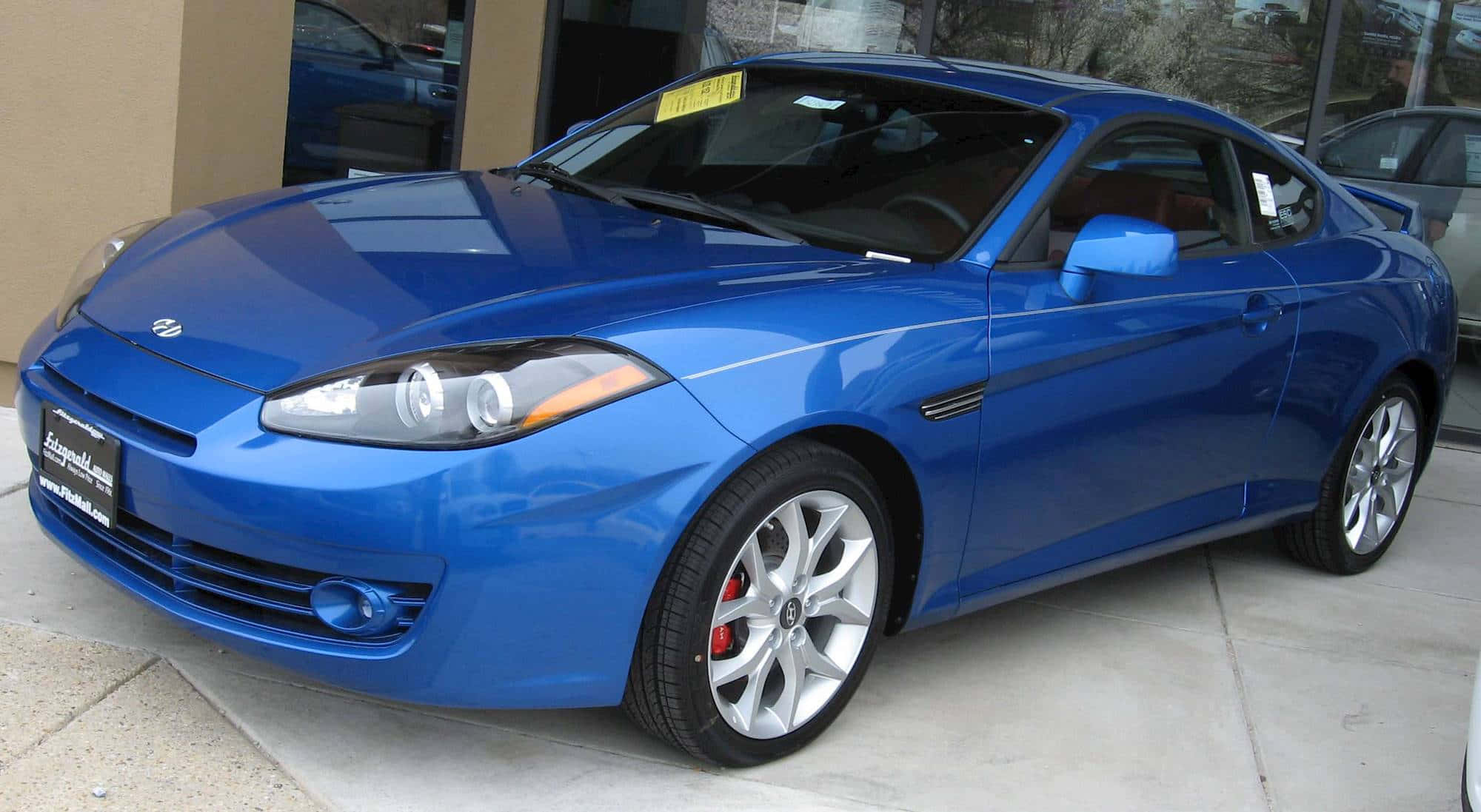 Hyundai Tiburon 桌布 壁紙 — 一輛光澤藍色運動轎跑車停在混凝土停車場上，配備銀色輪圈和紅色制動卡鉗。