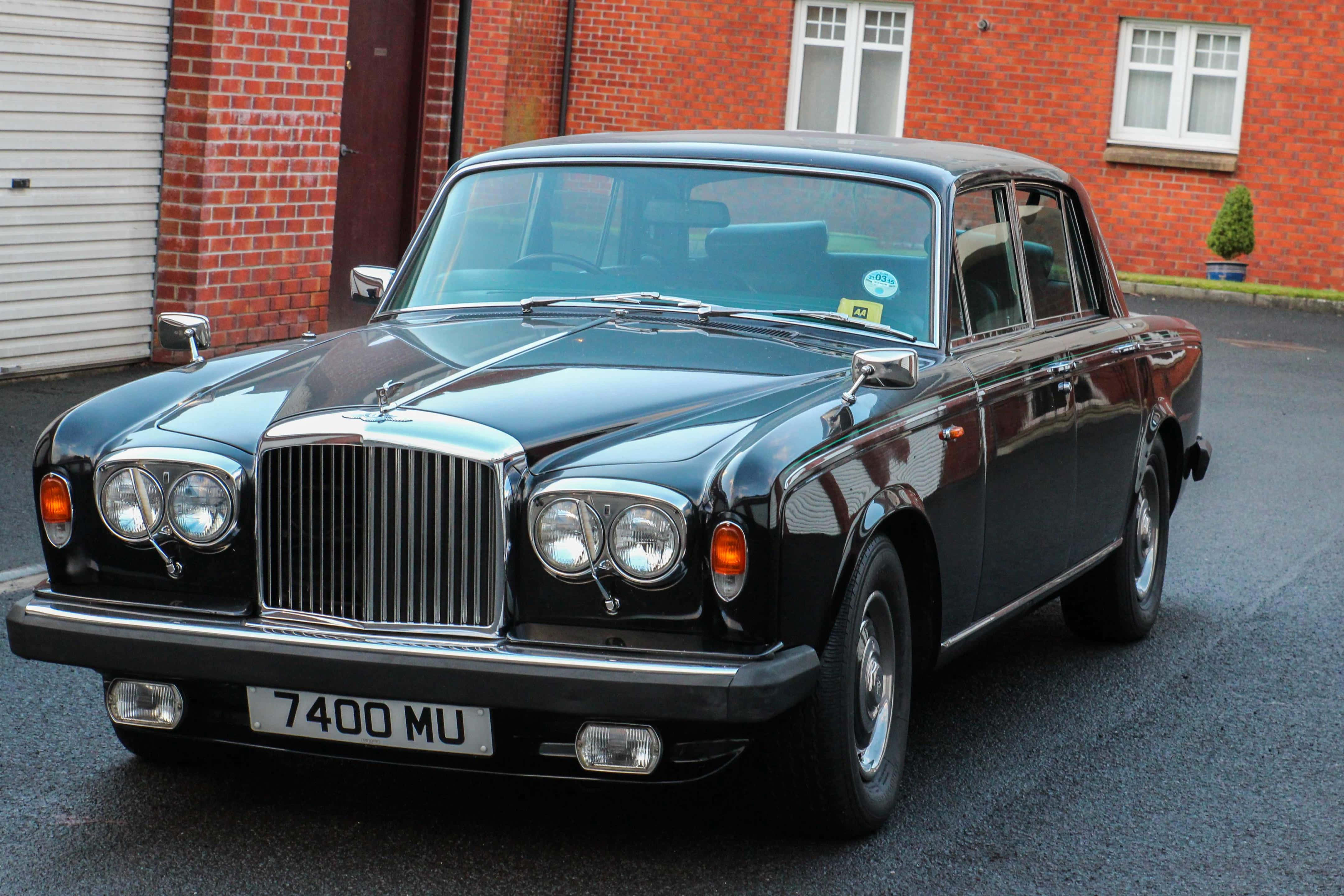 Bentley T2 桌布 壁紙 — 一輛光澤黑色經典賓利轎車停泊在紅磚建築前的瀝青路面上，建築物有白色窗戶。