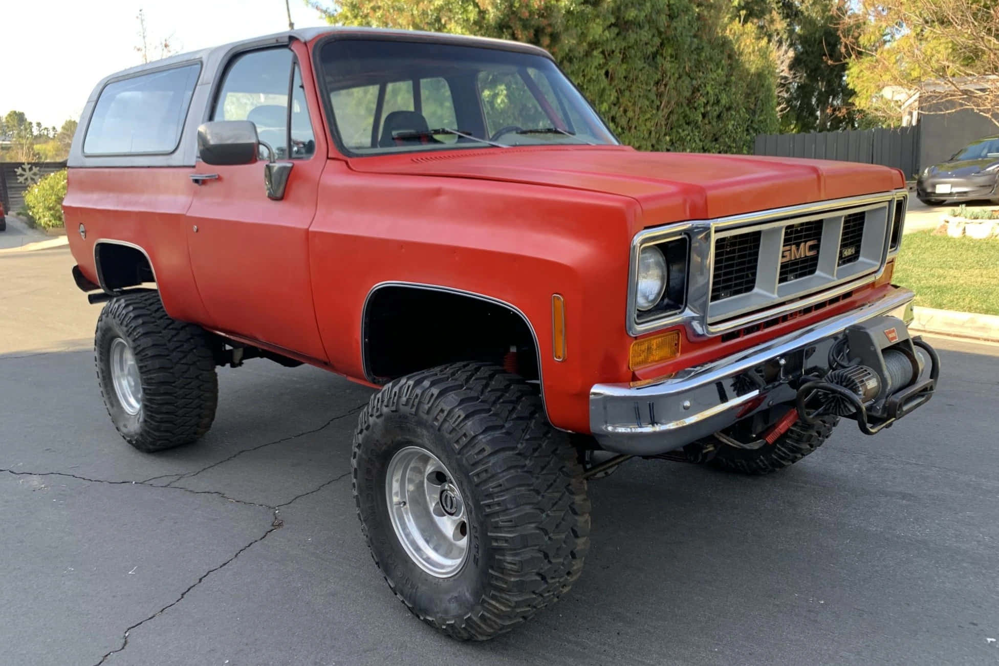 Gmc Jimmy 桌布 壁紙 — 一輛升高了的紅色GMC Jimmy SUV，配備大型越野輪胎，停泊在裂開的瀝青車道上。