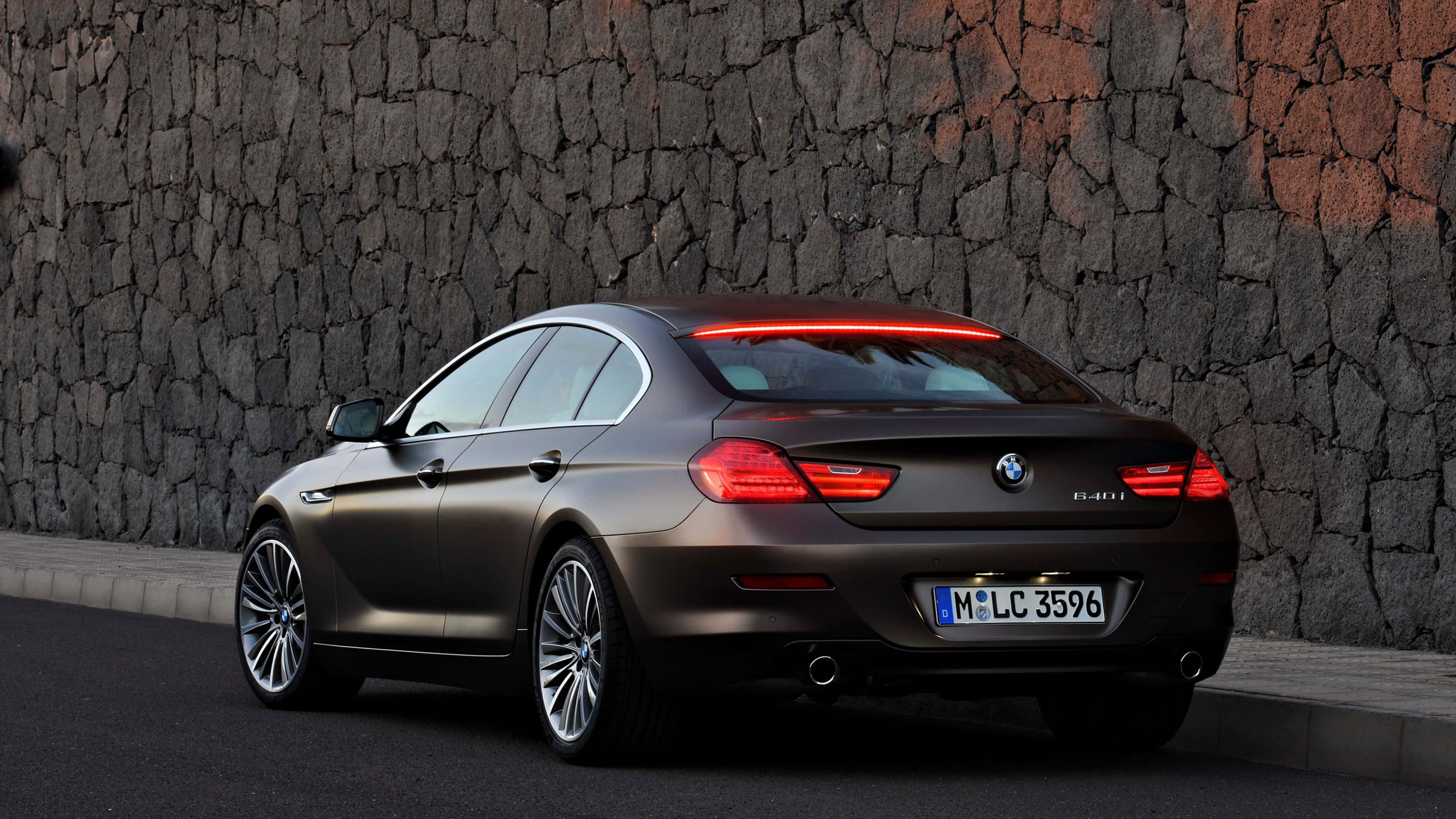 Bmw 6 Series 桌布 壁紙 — 一輛啞光啡色BMW 6系Gran Coupe停泊在粗糙石牆旁，紅色尾燈發亮。