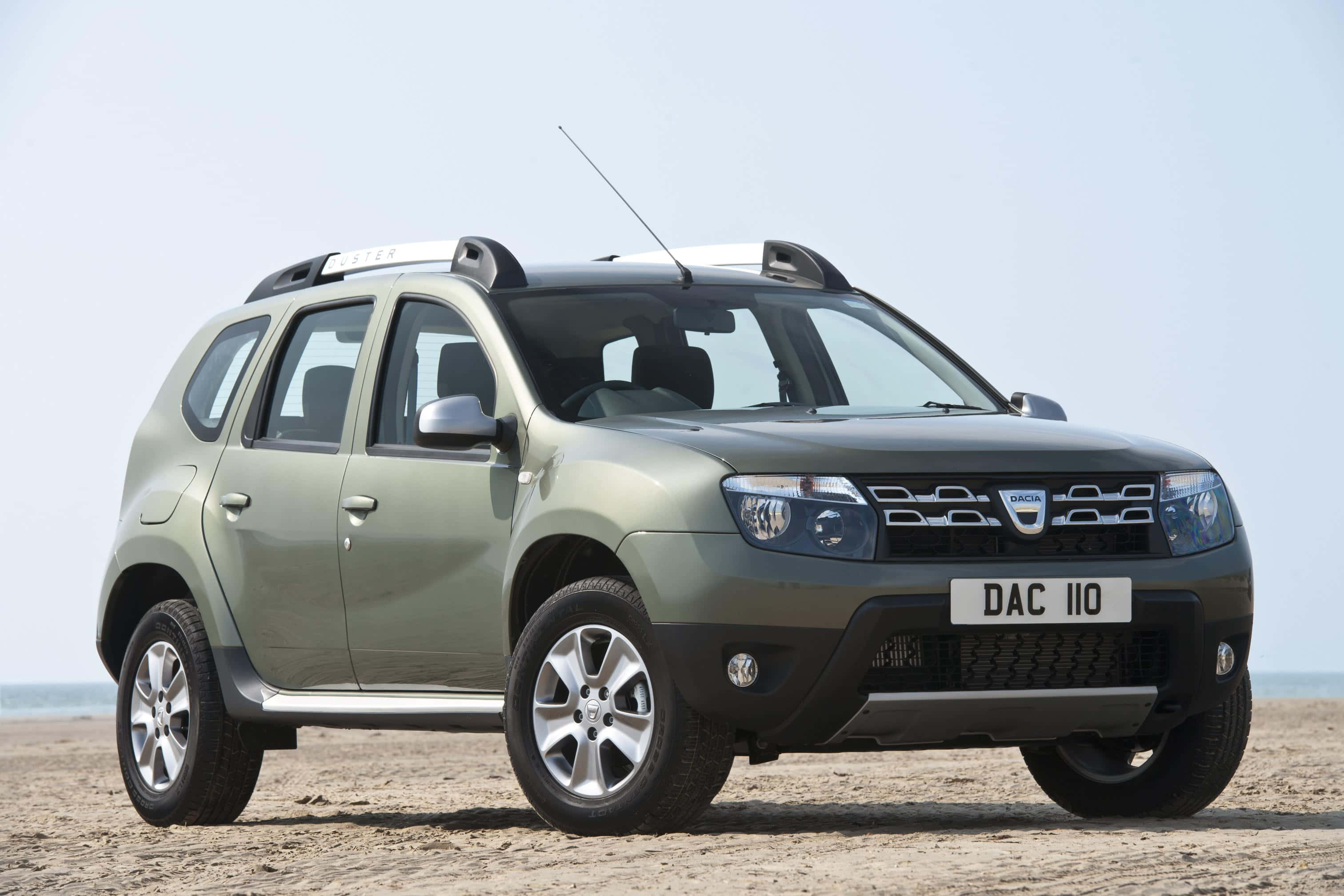 Dacia 桌布 壁紙 — 一輛啞光橄欖綠色的Dacia Duster SUV停泊在沙灘上，天空清澈淡藍。