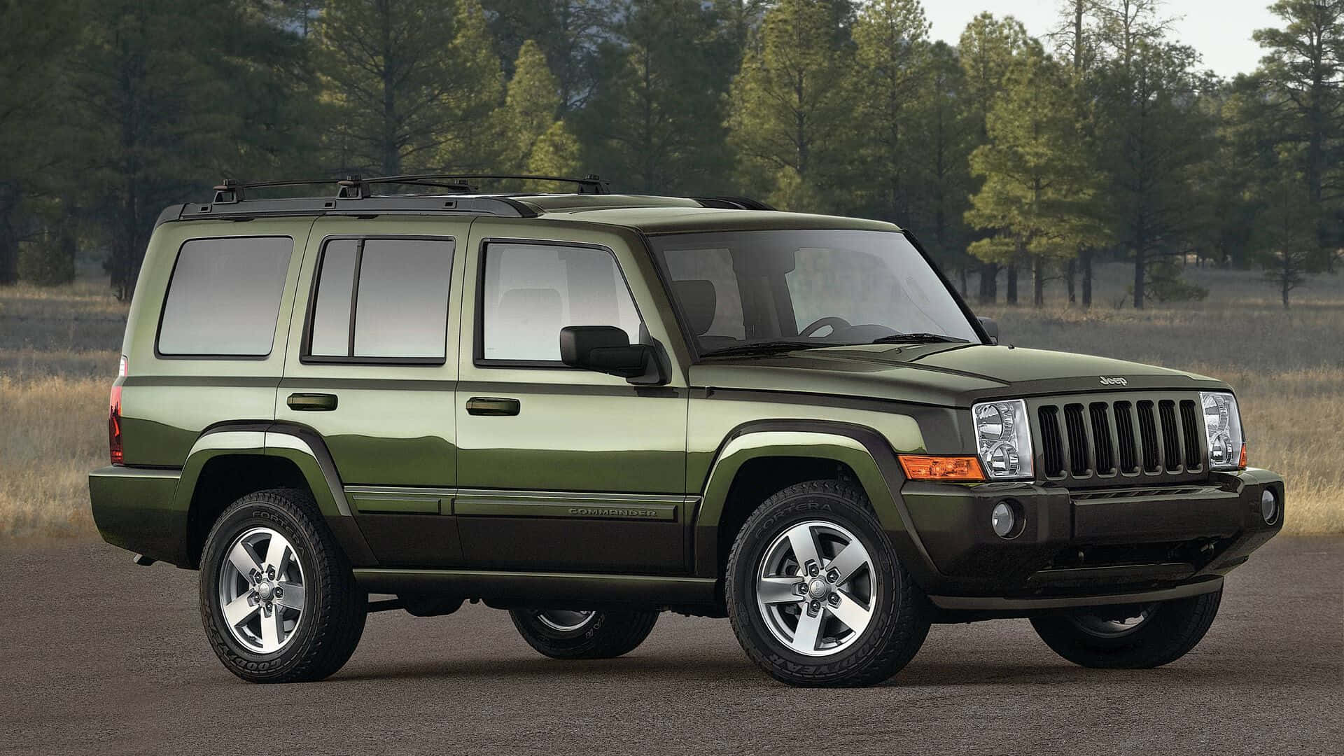 Jeep Commander 桌布 壁紙 — 一輛啞光橄欖綠色的Jeep Commander SUV停在瀝青路面上，背景是森林，光線柔和。