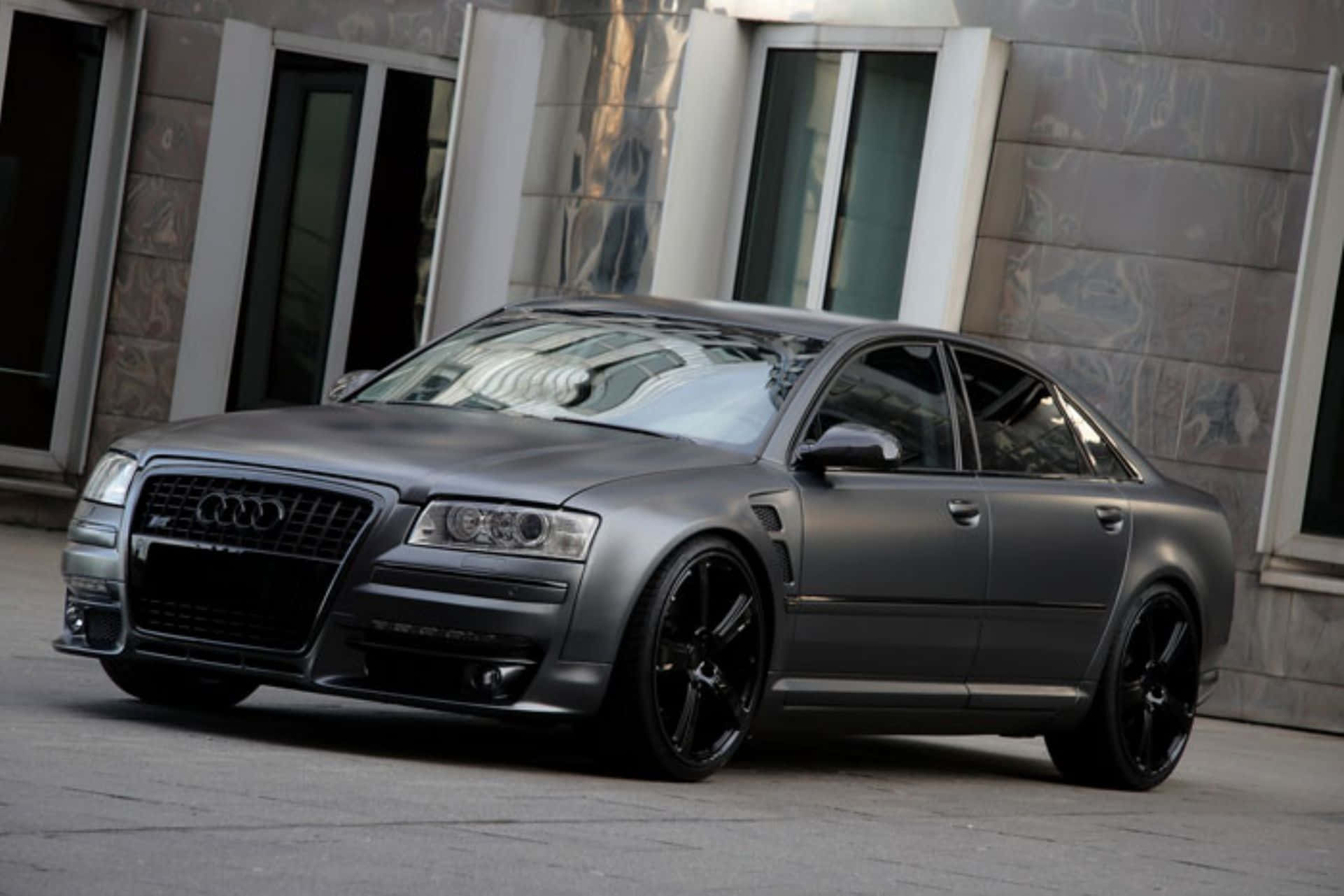 Audi S8 桌布 壁紙 — 一輛啞光灰色奧迪轎車配黑色輪圈，停在一棟帶有反光玻璃的現代建築前。