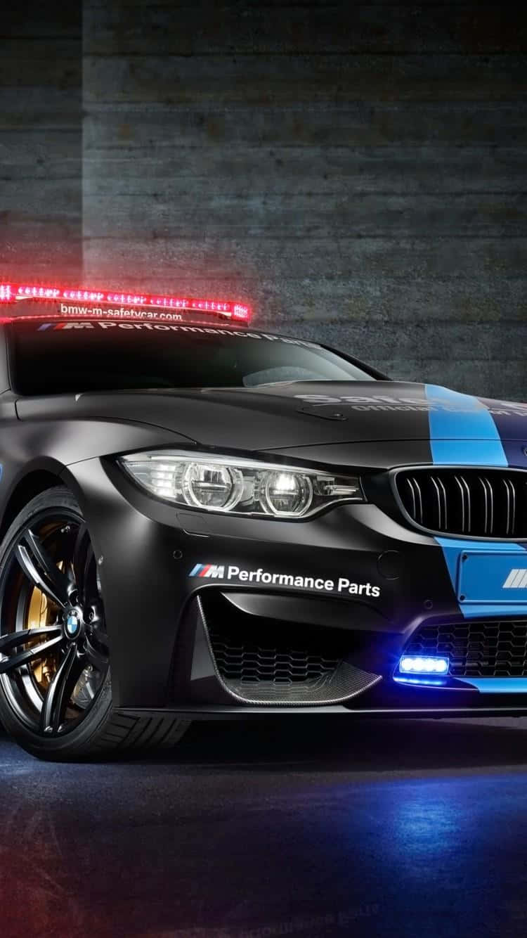 Safety Car 桌布 壁紙 — 一輛啞光黑色BMW M4安全車，帶有藍色賽車條紋和紅色車頂燈，在戲劇性的工作室燈光下閃耀。