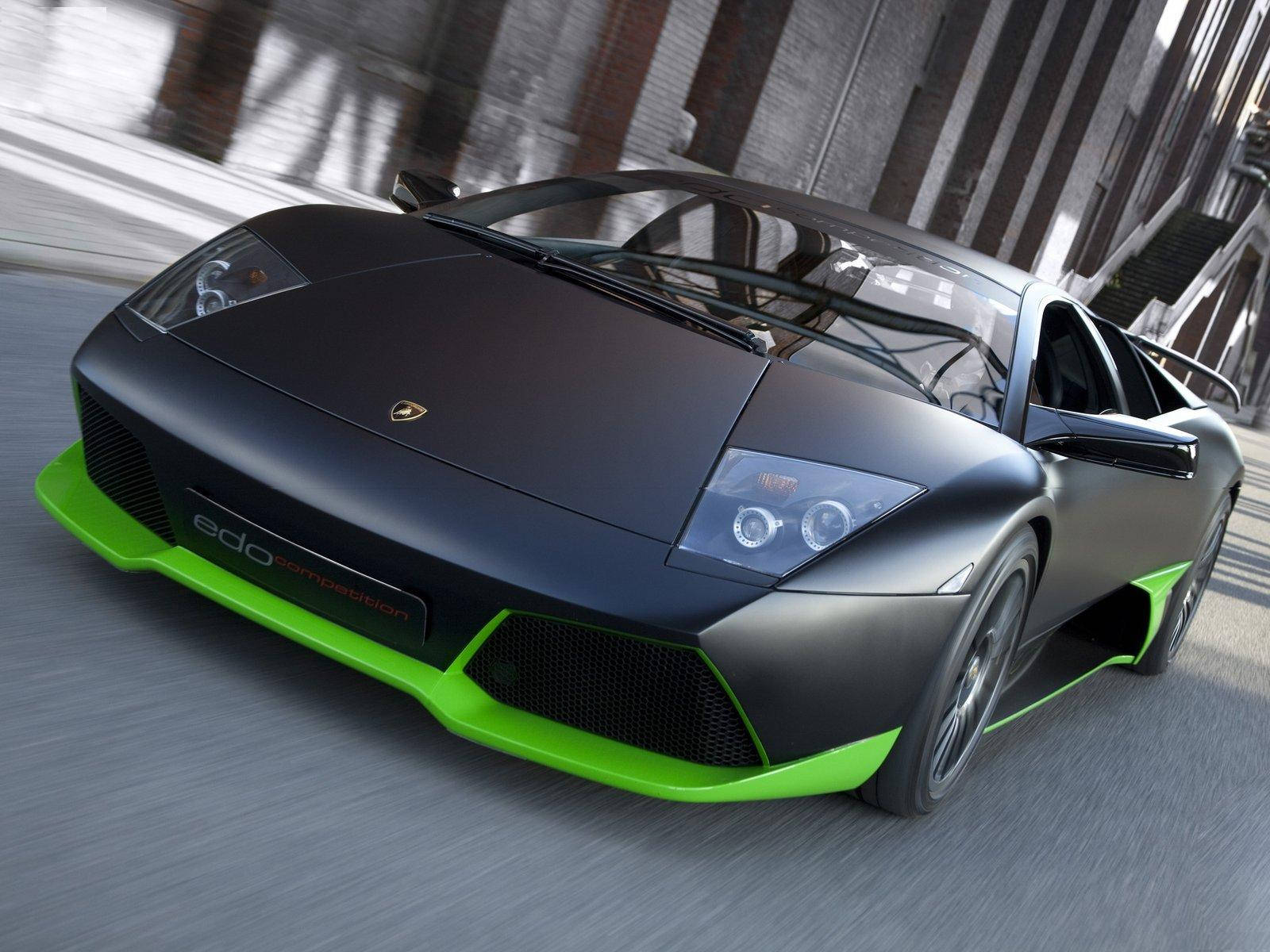 Sports Car 桌布 壁紙 — 一輛啞光黑色林寶堅尼帶有螢光綠色點綴，在模糊的城市街道峽谷中疾馳。