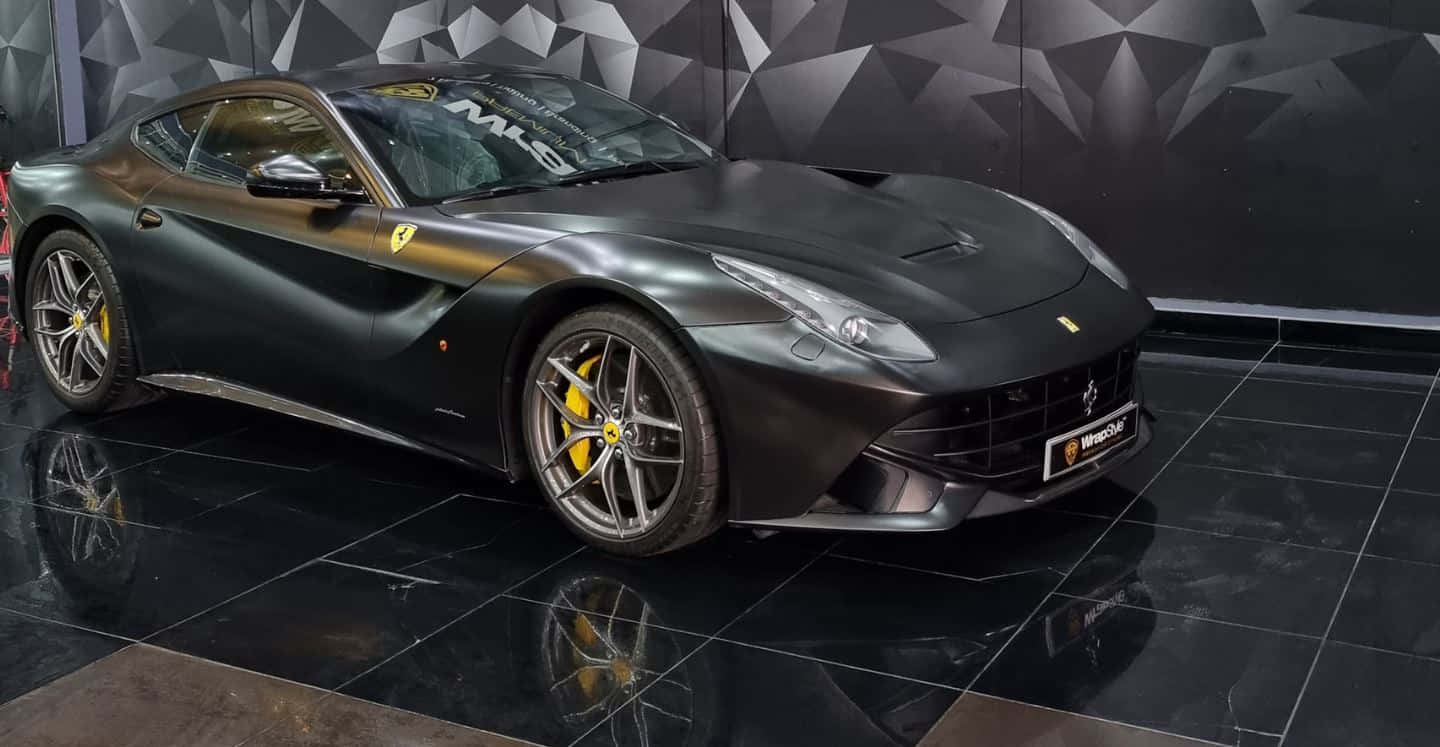 Ferrari F12 Berlinetta 桌布 壁紙 — 一輛啞光黑色法拉利F12tdf跑車配黃色制動卡鉗，展示在光面黑色瓷磚地板上，背景為幾何牆壁。