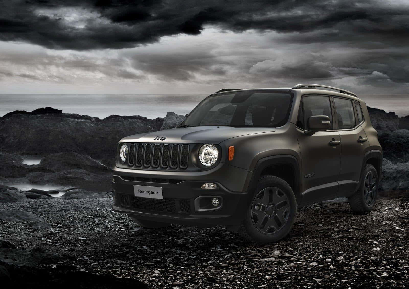 Jeep Renegade 桌布 壁紙 — 一輛啞光黑色的Jeep Renegade堅固地矗立在岩石海岸上，頭上是暴風雨前的灰色天空，海浪拍打著岸邊。