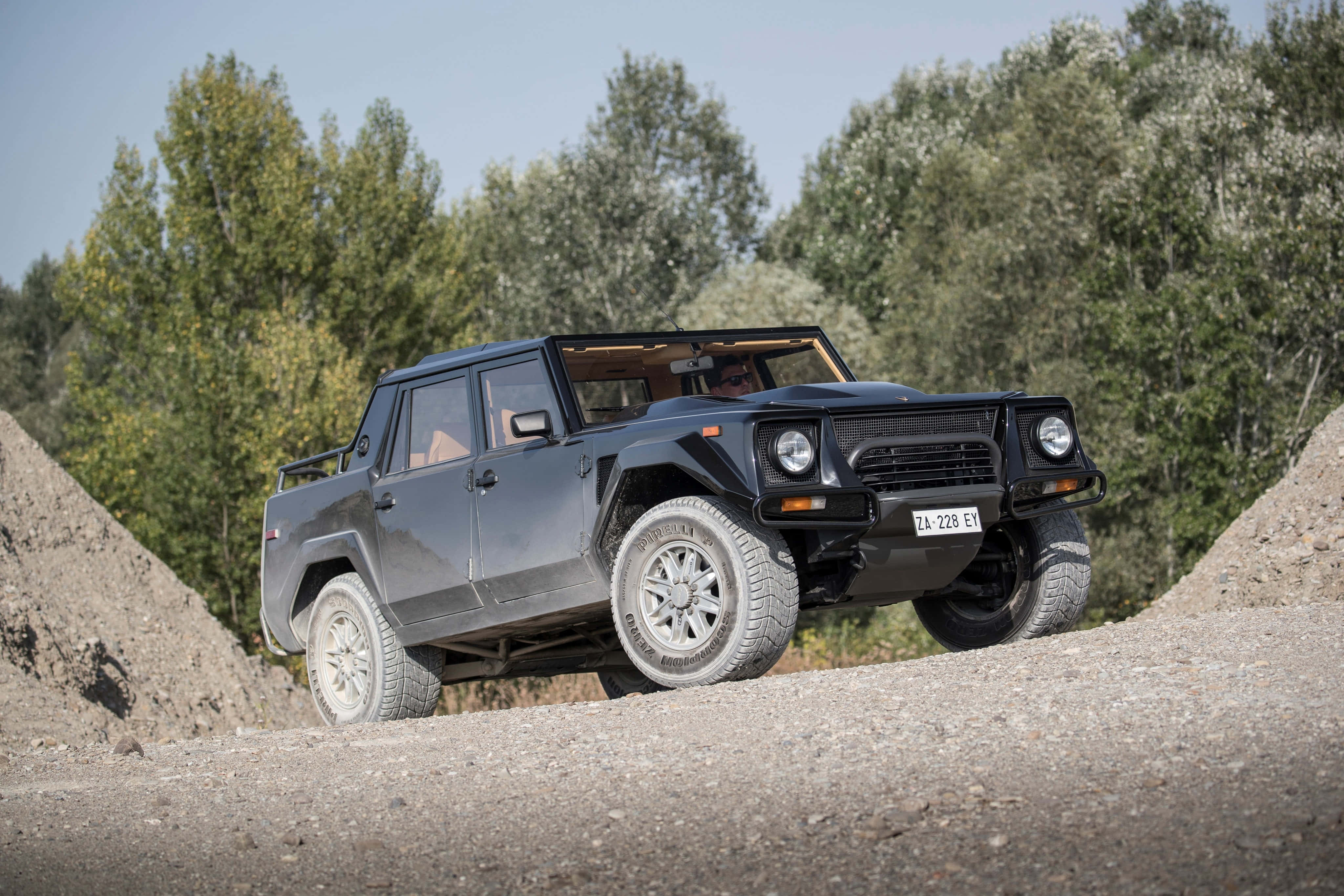 Lamborghini Lm002 桌布 壁紙 — 一輛啞光黑色的林寶堅尼LM002 SUV在晴朗的藍天下，以堅固的輪胎和霸氣的姿態征服陡峭的碎石坡。