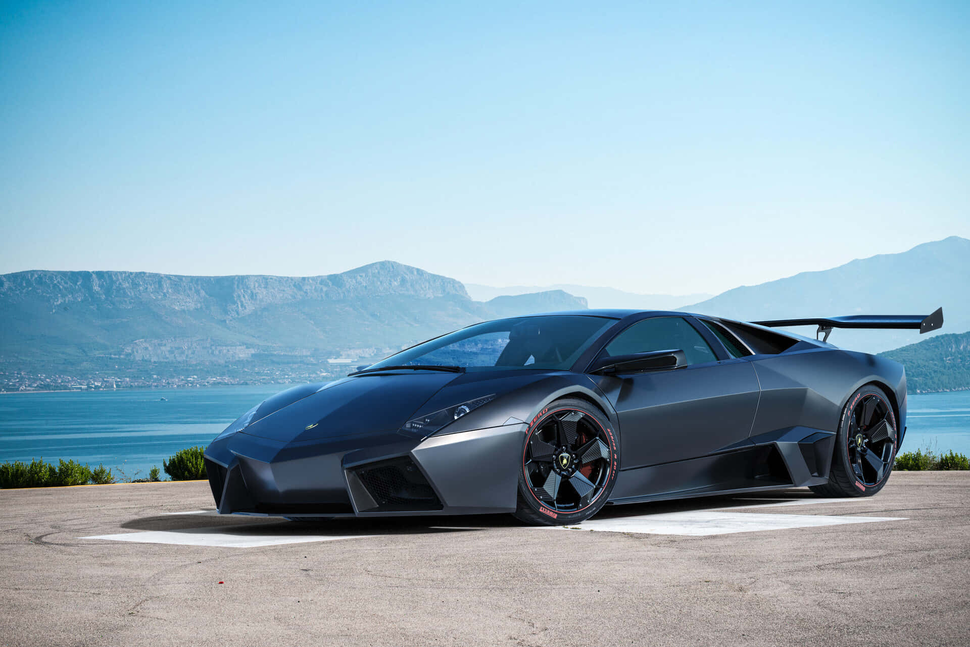 Lamborghini Reventón 桌布 壁紙 — 一輛啞光黑色的林寶堅尼Reventon跑車停泊在沿海公路上，背景是山脈和藍色海洋。