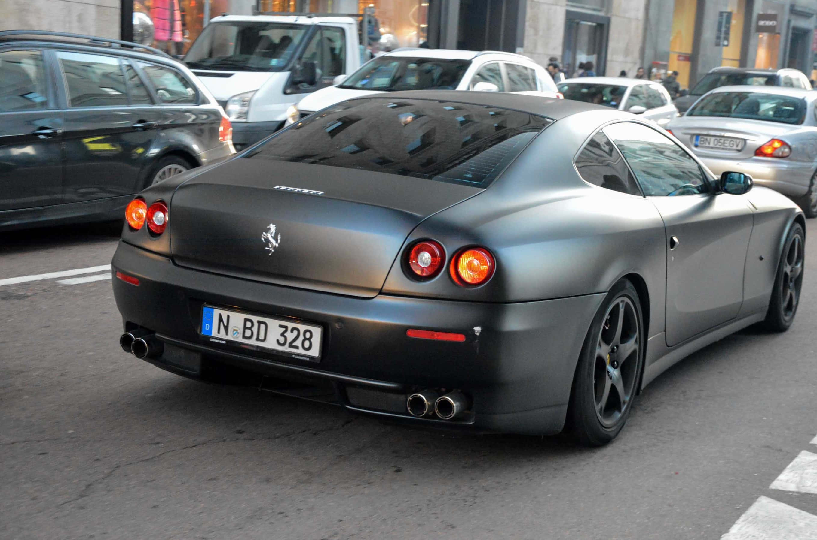 Ferrari 612 Scaglietti 桌布 壁紙 — 一輛啞光黑色的法拉利612 Superamerica停在繁忙的城市街道上，紅色尾燈閃閃發光。
