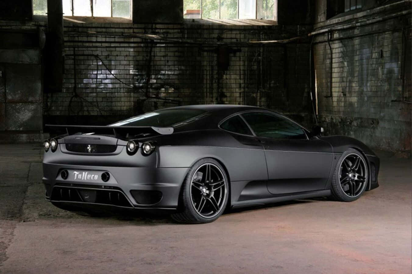Ferrari F430 桌布 壁紙 — 一輛啞光黑色的法拉利跑車配備定制輪圈，戲劇性地停放在昏暗骯髒的工業倉庫中。