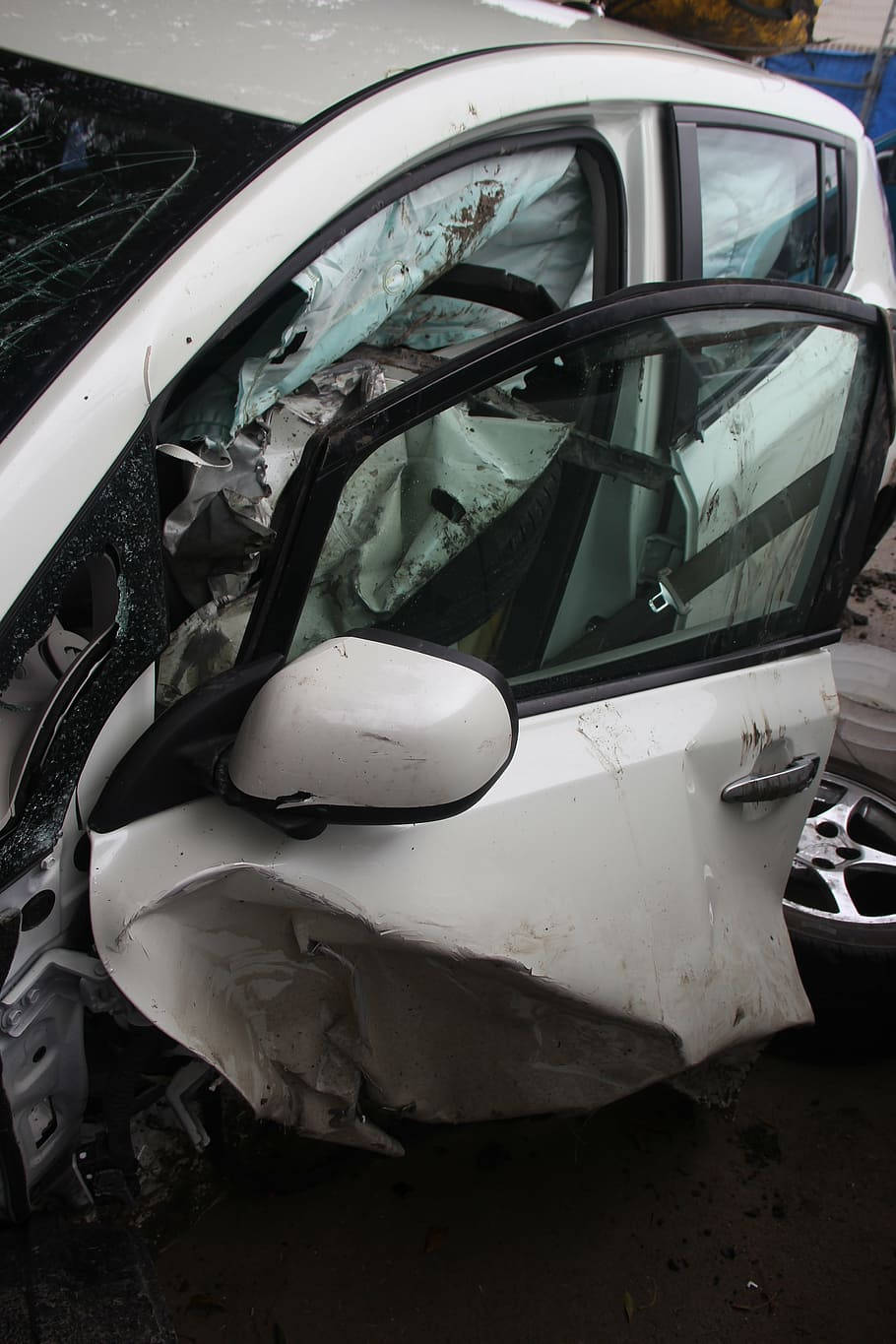 car crash 桌布 壁紙 — 一輛嚴重損毀的白色汽車，車窗破碎，前門被壓碎，停在廢車場。