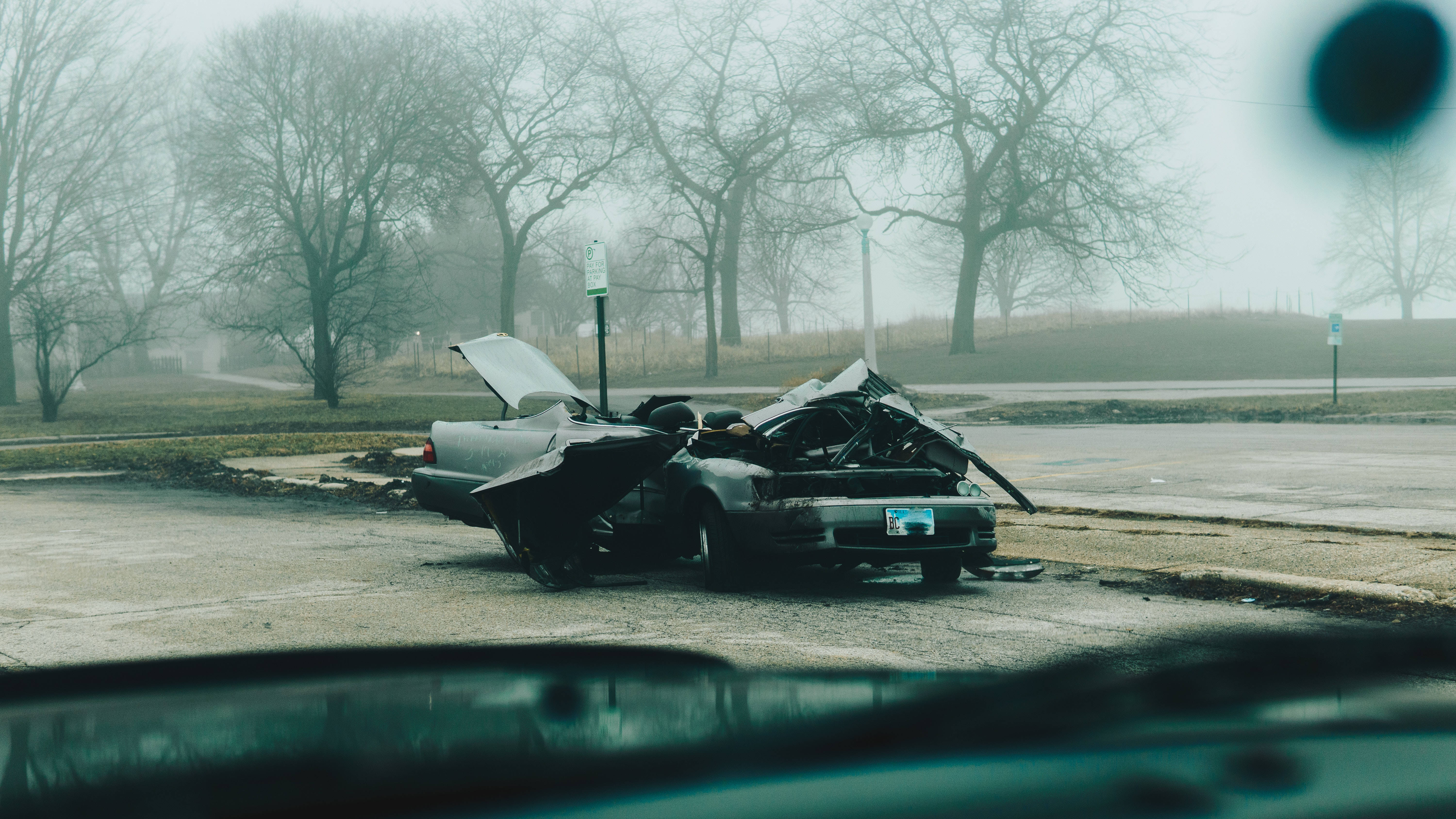 Car Accident 桌布 壁紙 — 一輛嚴重損毀的銀色汽車被遺棄在霧氣瀰漫的停車場，周圍是光禿禿的樹木。