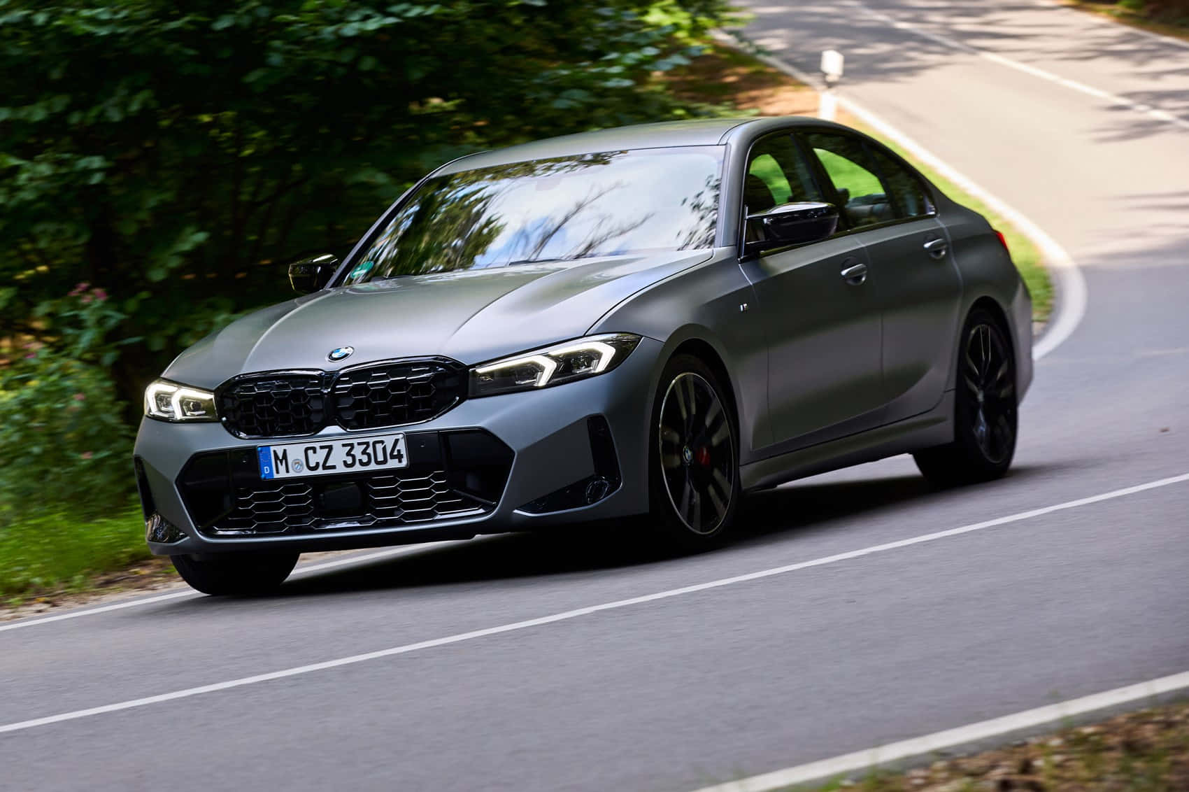 Bmw 3 Series 桌布 壁紙 — 一輛型格啞光灰色BMW 3系房車在蜿蜒的森林道路上行駛，兩旁綠樹成蔭。