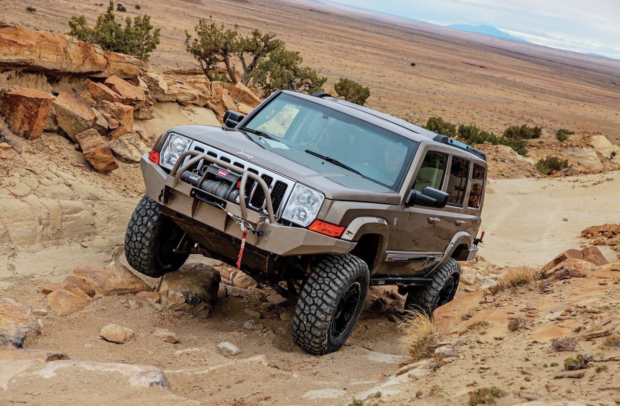 Jeep Commander 桌布 壁紙 — 一輛堅固的棕褐色Jeep Wrangler配備超大輪胎，在廣闊的天空下征服岩石沙漠小徑。