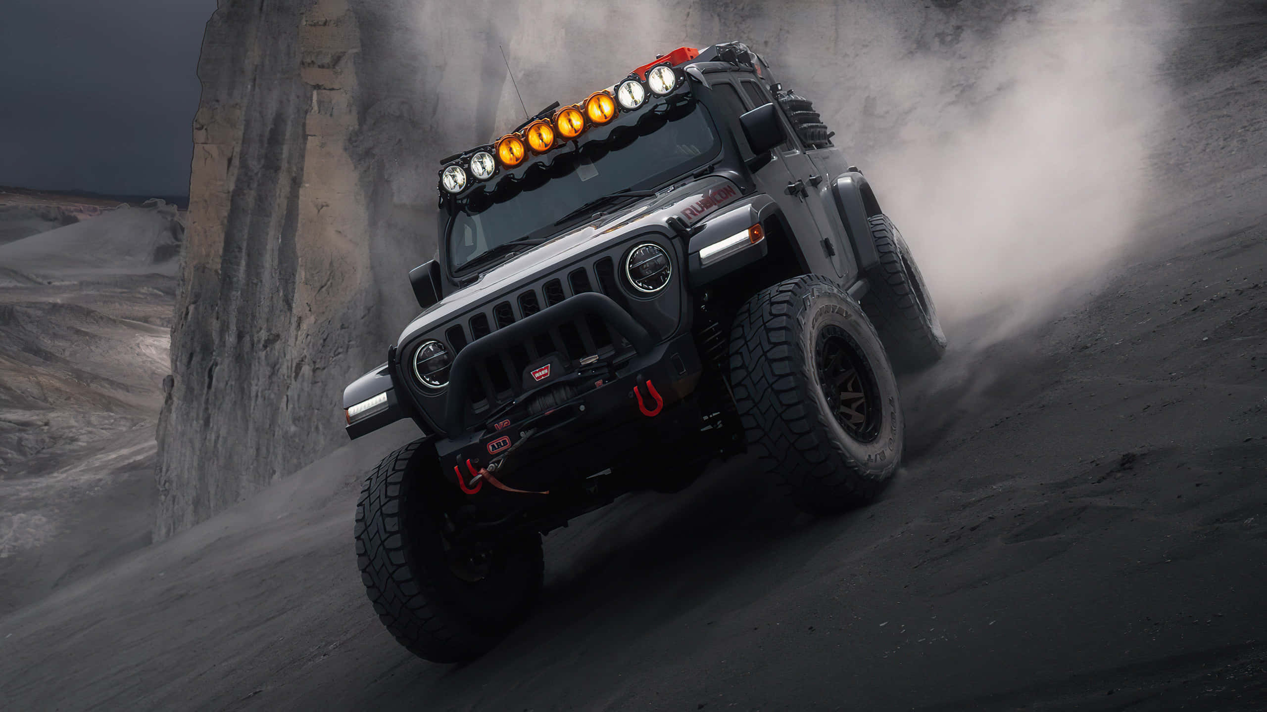 Jeep 動圖 桌布 壁紙 — 一輛堅固的黑色Jeep Wrangler帶着橙色燈光，在暴風雨的天空下攀爬陡峭的岩石斜坡，揚起灰塵。