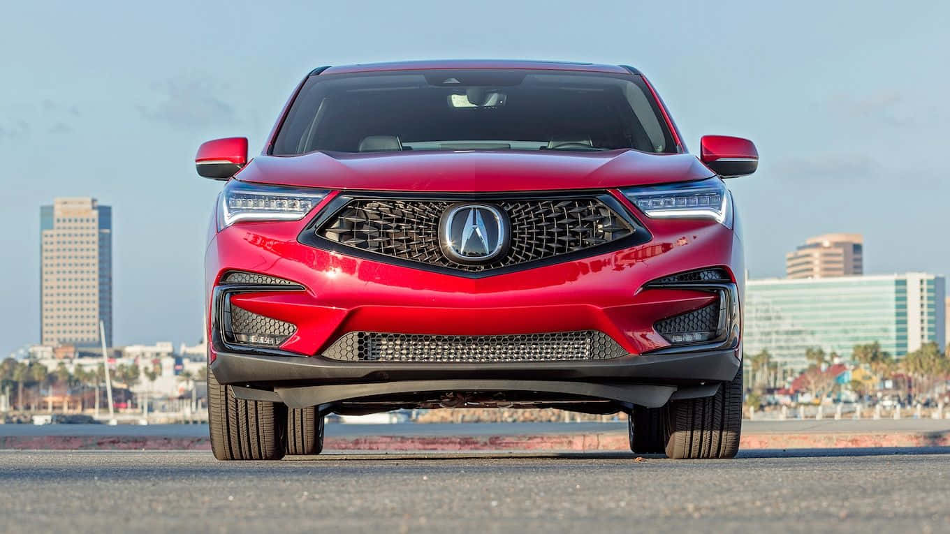 Acura Rdx 桌布 壁紙 — 一輛大膽的紅色Acura SUV在濱海道路上向前行駛，背景是城市摩天大樓和棕櫚樹，天空晴朗。