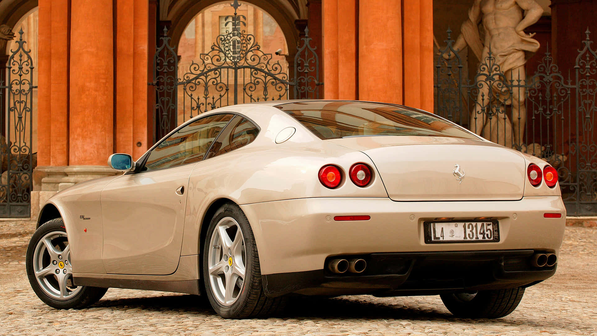 Ferrari 612 Scaglietti 桌布 壁紙 — 一輛奶油色法拉利612 Superamerica停泊在鵝卵石路上，前面是華麗的鐵門和古典雕像。